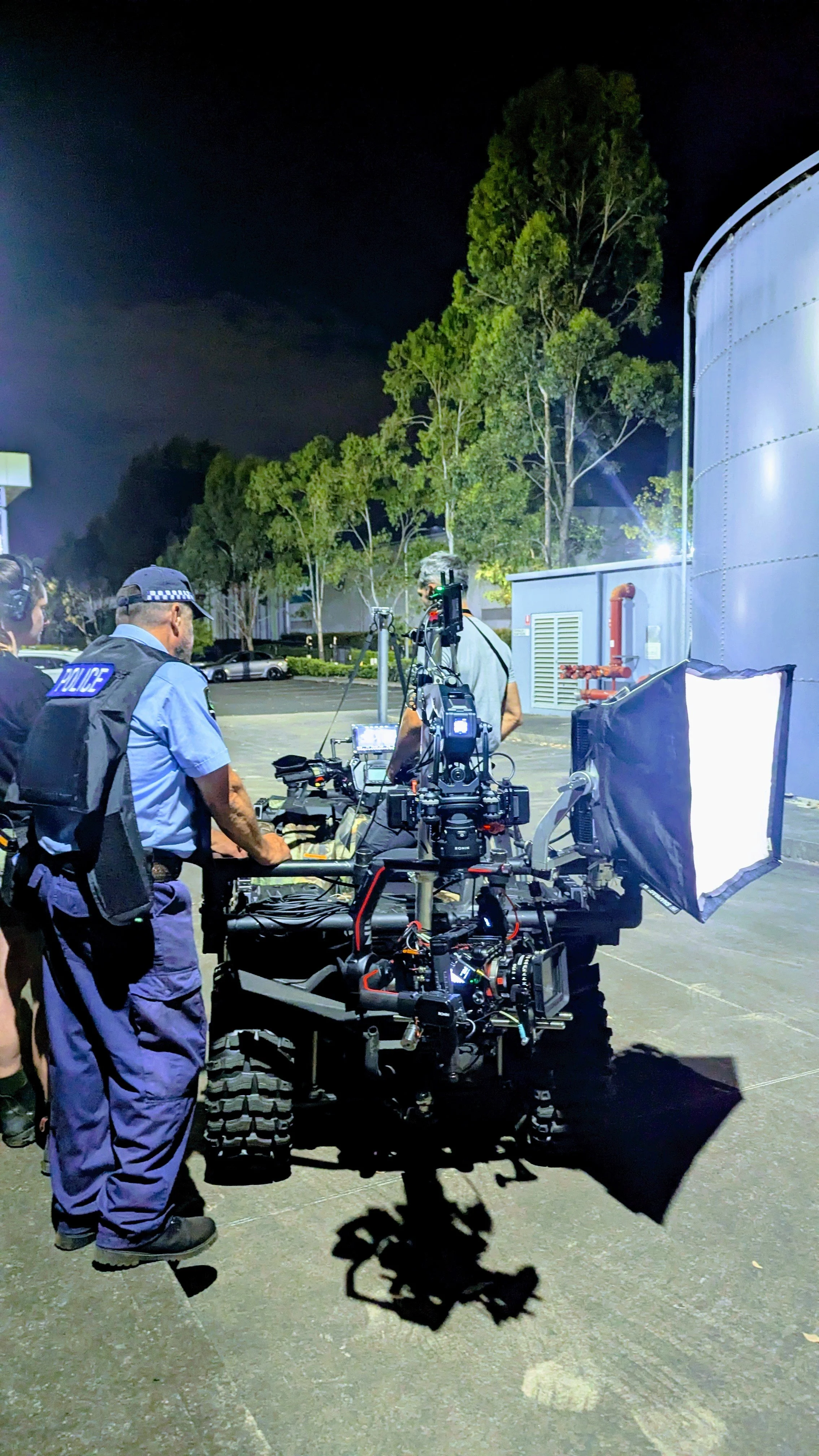 Nighttime scene with police officers operating a professional camera on a rugged vehicle, with large lights and trees in the background.