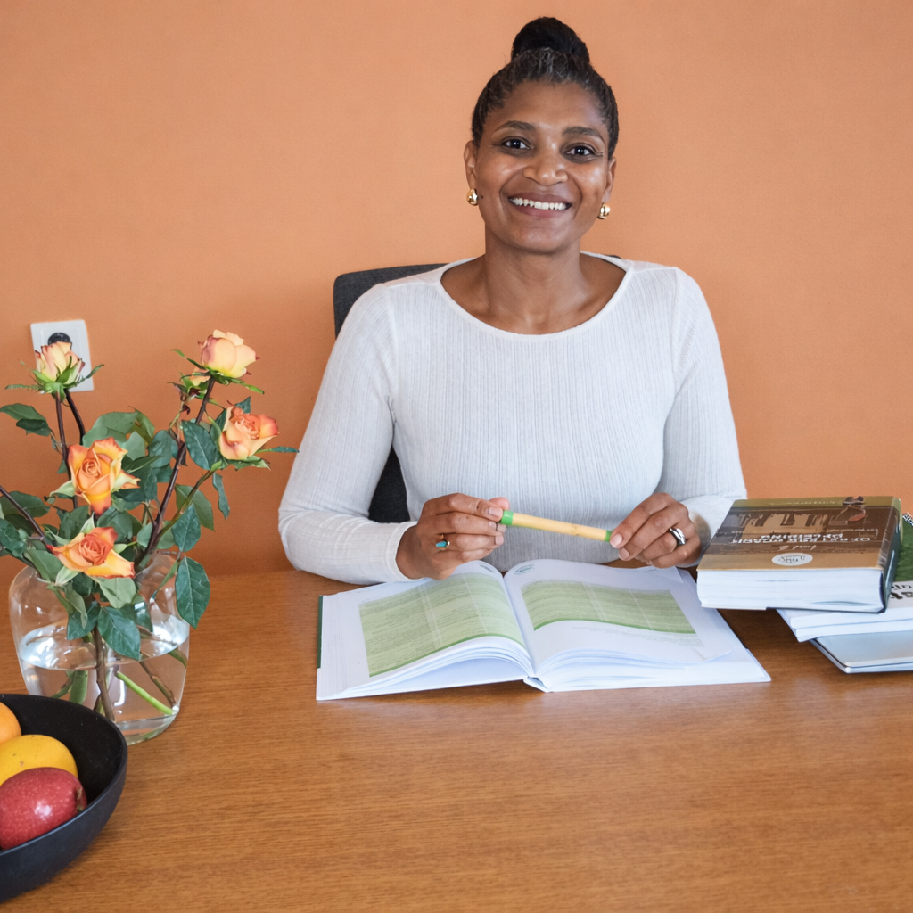 Fátima, leefstijlcoach, zit aan tafel met een open boek en aantekeningen, klaar om je te begeleiden met leefstijlcoaching.