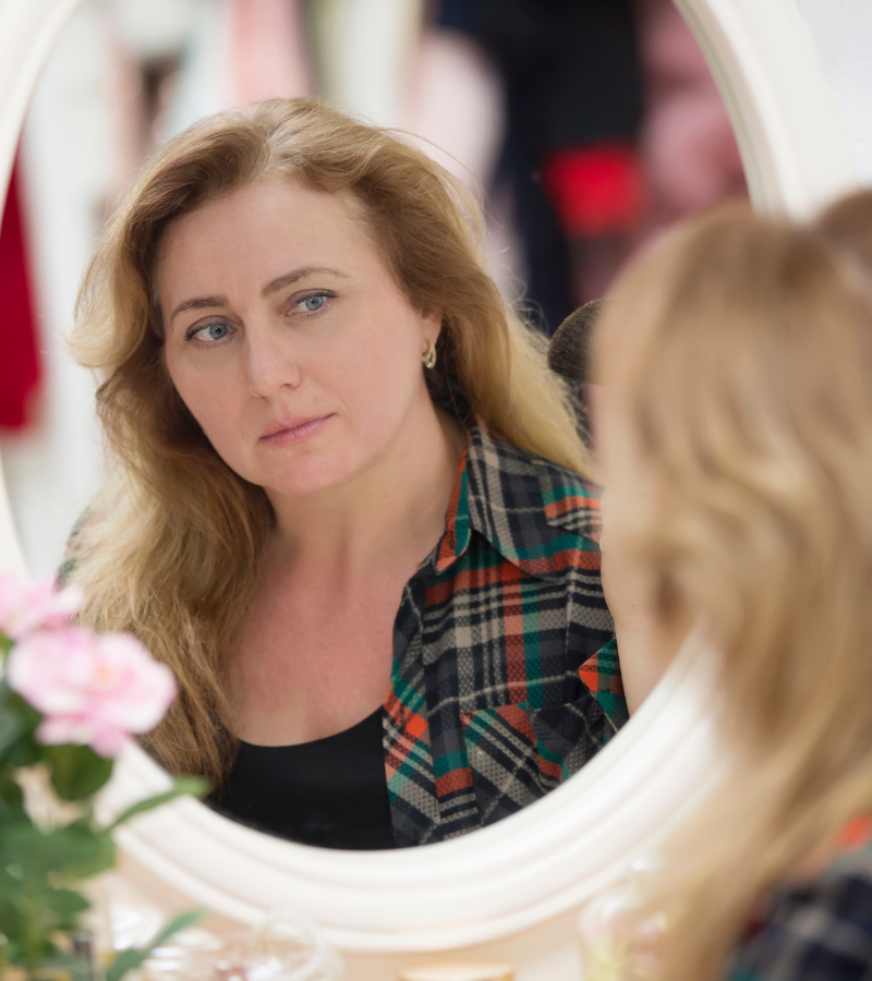 Vrouw kijkt in de spiegel als symbool voor zelfvertrouwen en persoonlijke leefstijlverandering.