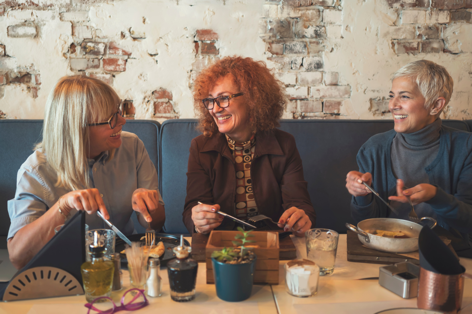Drie vrouwen praten en lachen aan tafel; meer energie, rust en zelfvertrouwen door leefstijlcoaching.