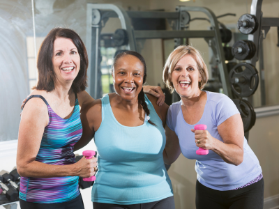 Drie vrouwen in sportkleding met gewichten, energiek en samen werken aan een gezondere leefstijl.