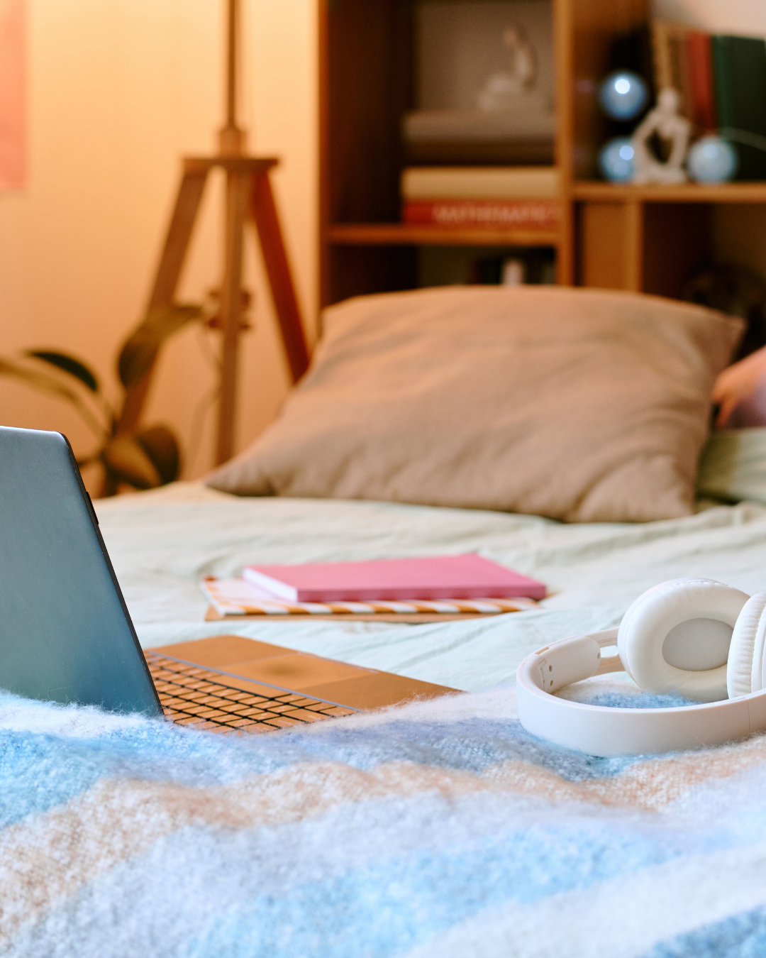 Laptop op een bed met koptelefoon en notitieboek; beeld voor online leren en begeleiding in de community.