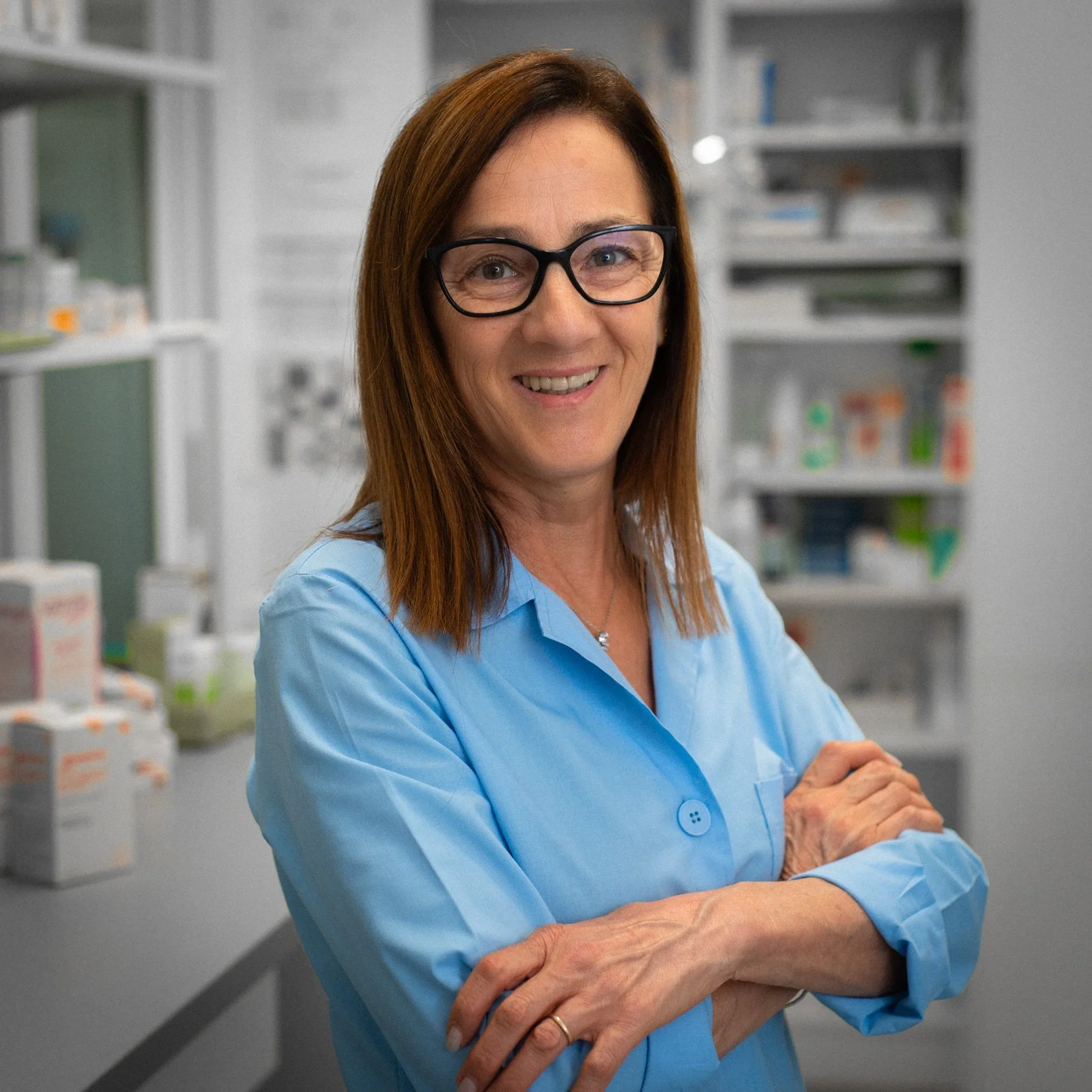 Donna sorridente con camice blu in laboratorio. Packaging di farmaci e attrezzature sullo sfondo.