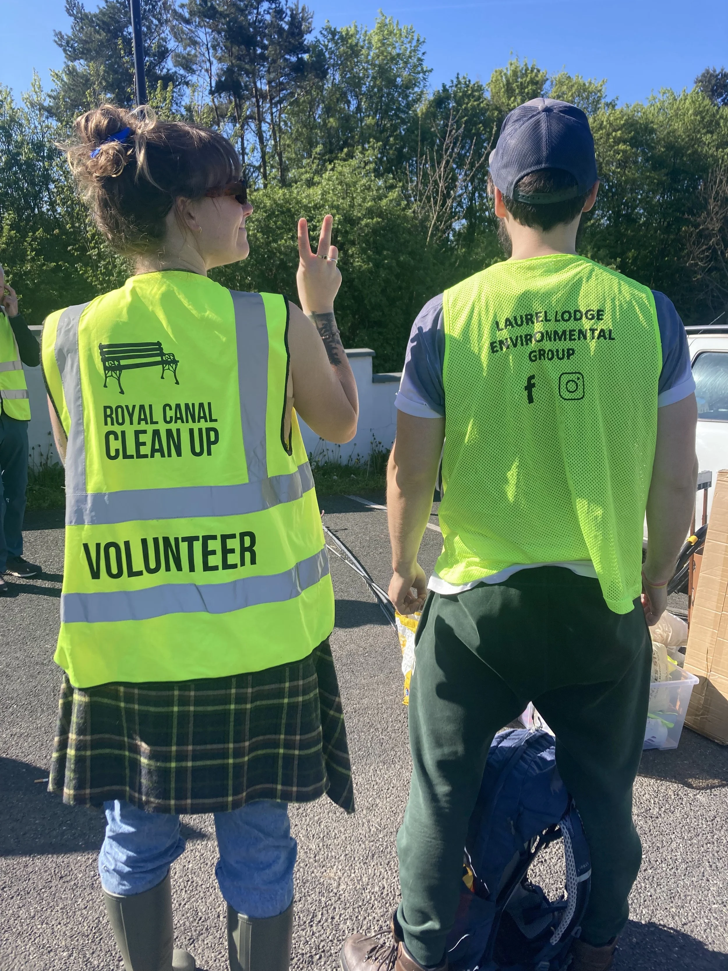 Two Monster Clean Up volunteers wearing bright yellow vests at an outdoor cleanup event. 