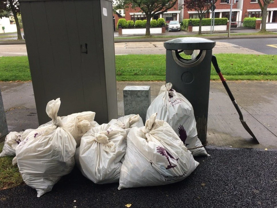 Litter picking bags filled with garbage piled next to a trash in Laurel Lodge