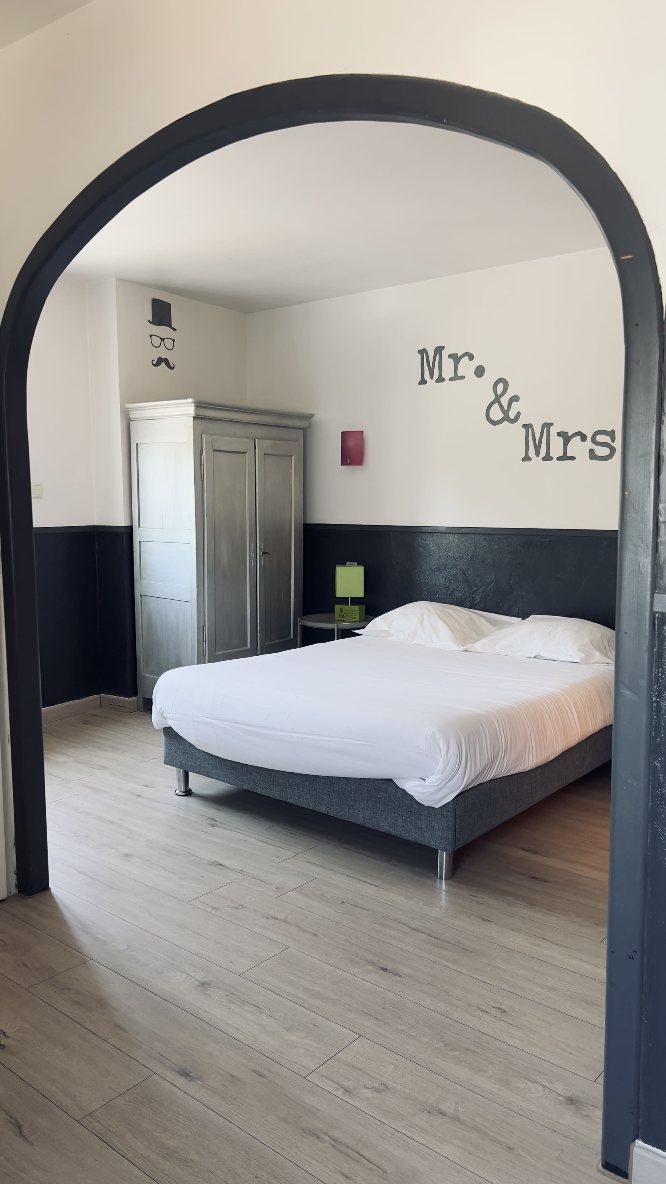 Chambre avec un lit double, armoire en bois, et décorations murales "Mr. & Mrs.".