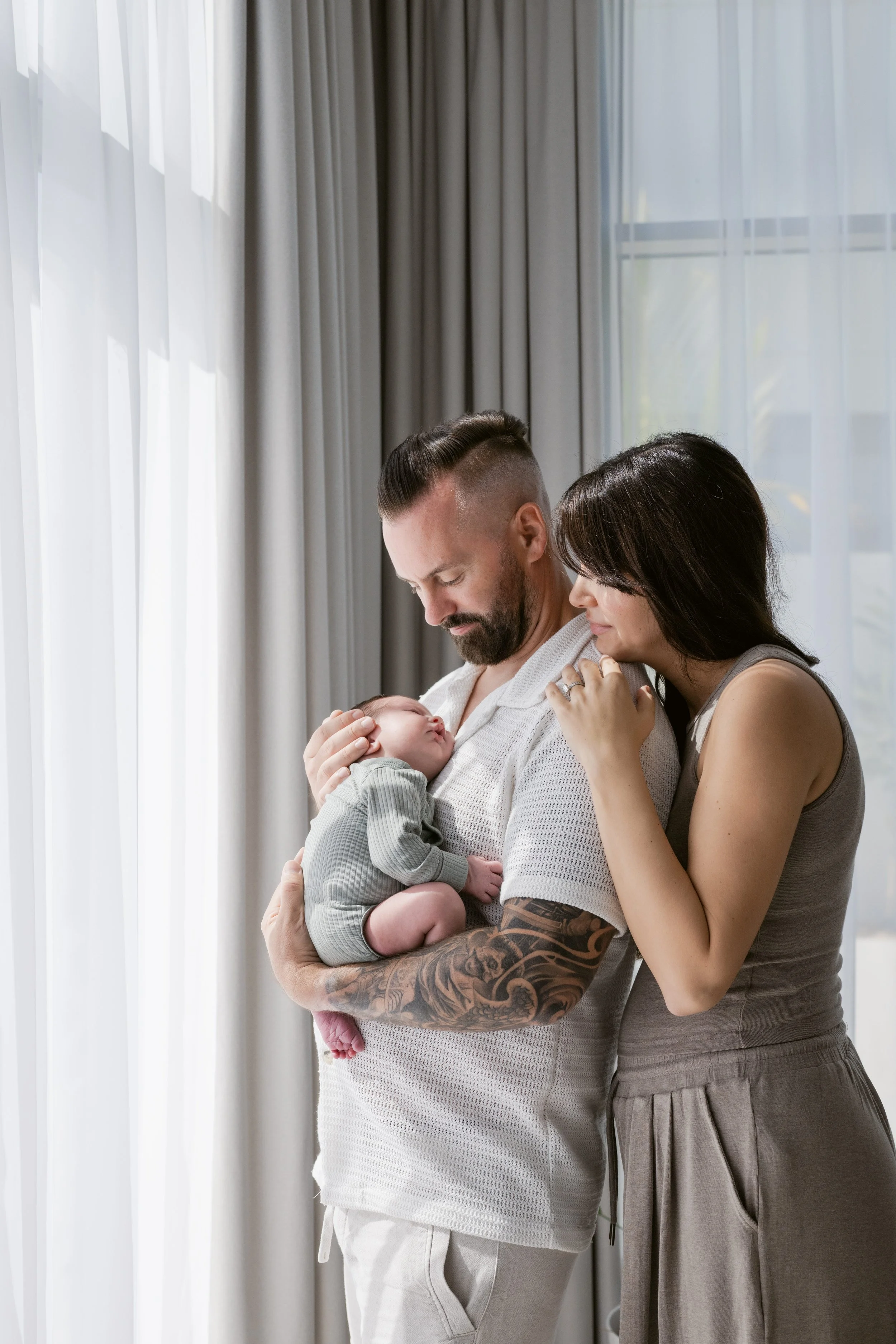 Parents holding their newborn beside a window during a lifestyle newborn photography session in Dubai