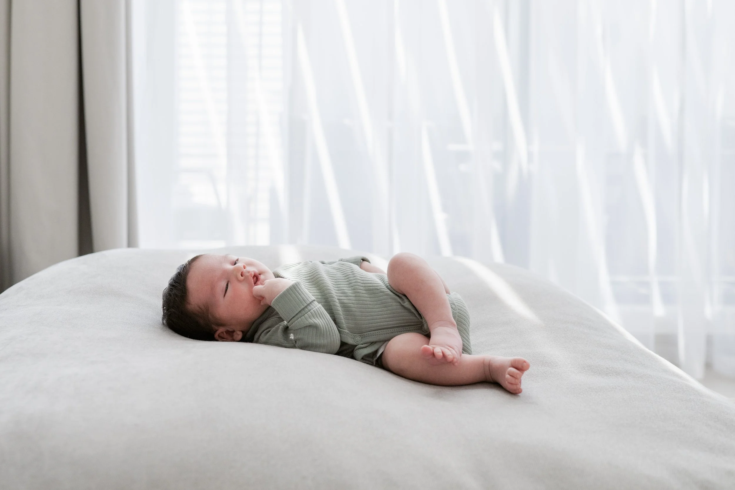 Newborn baby lying on a bed in soft natural light during a newborn home session in Dubai