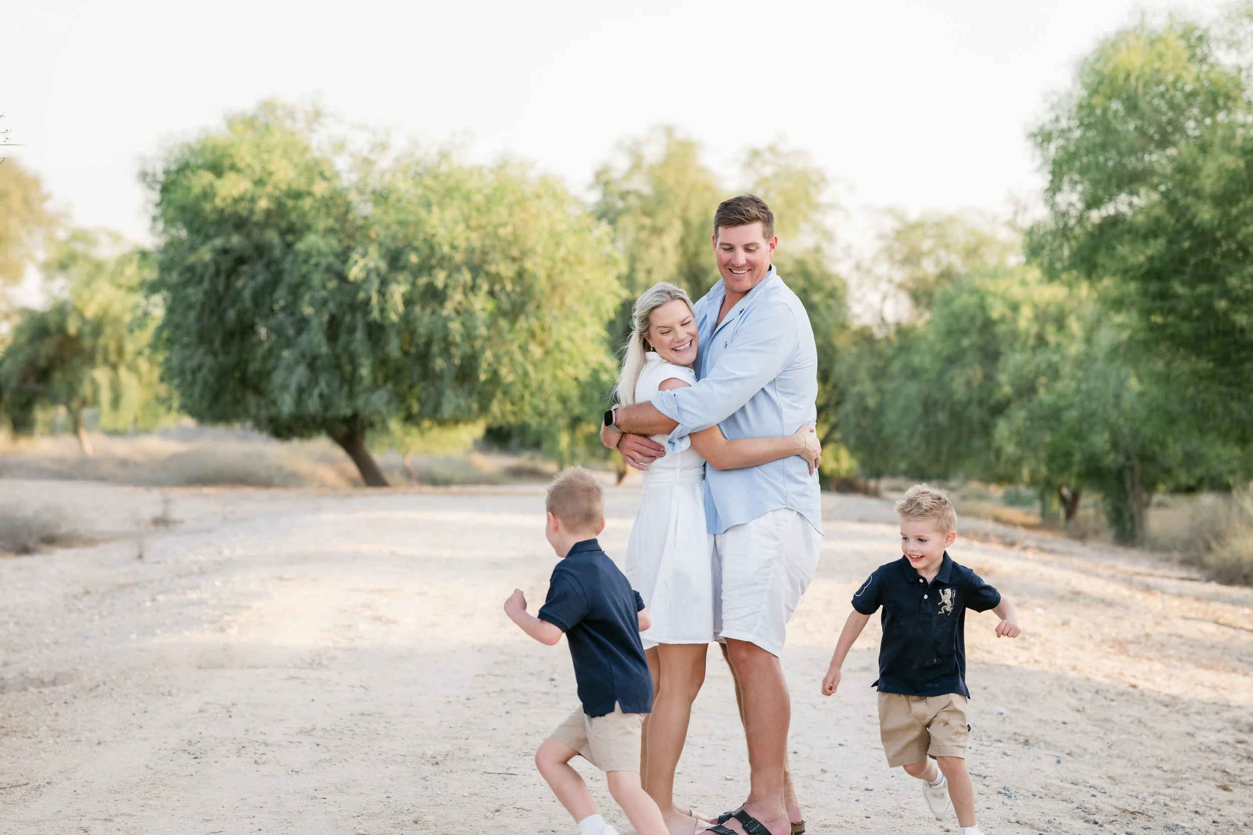 Parents hugging during a relaxed family session at Al Qudra Lakes, Dubai, while the kids are running around them happily.