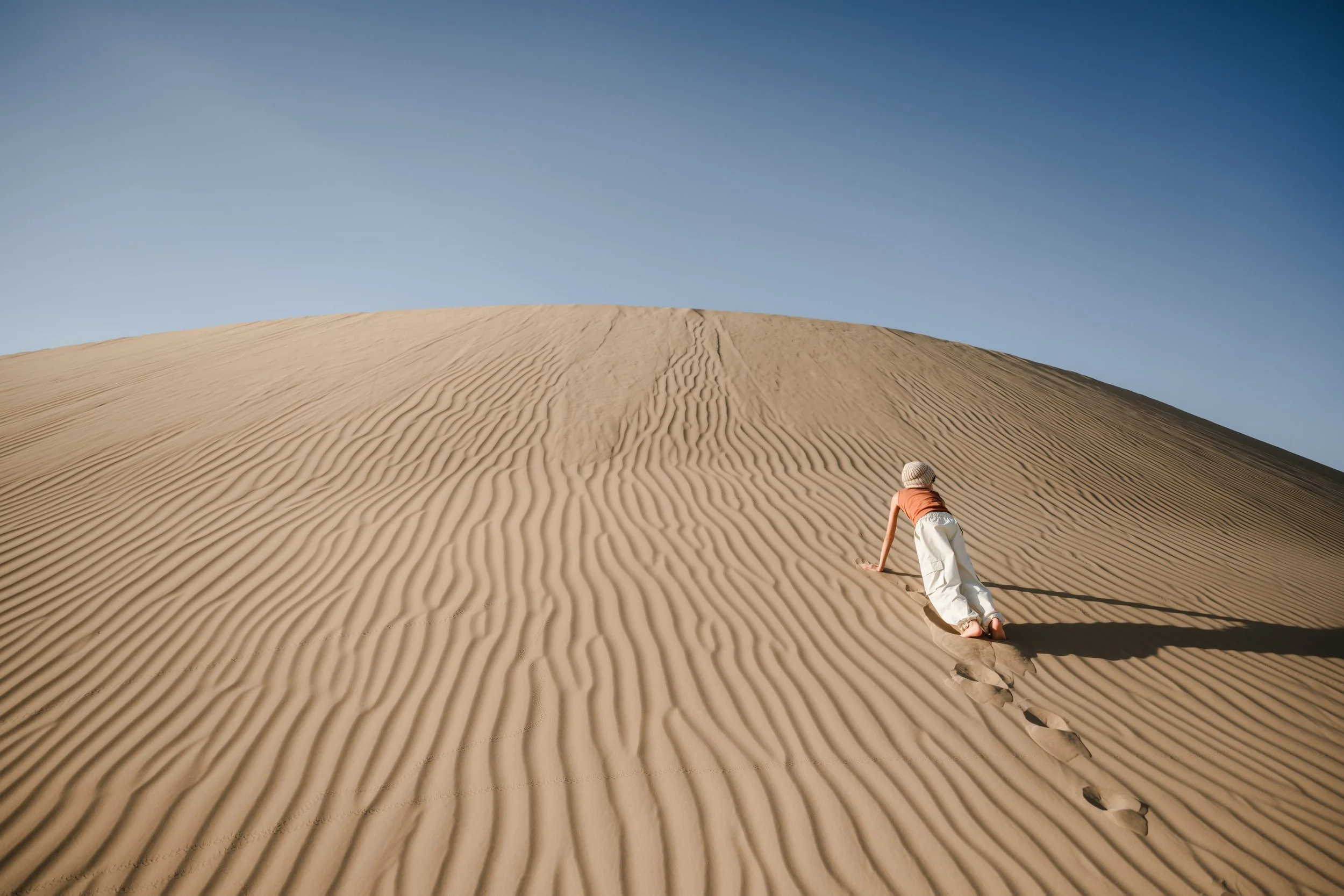 A boy on a sandy dune in Dubai, looking at his side.