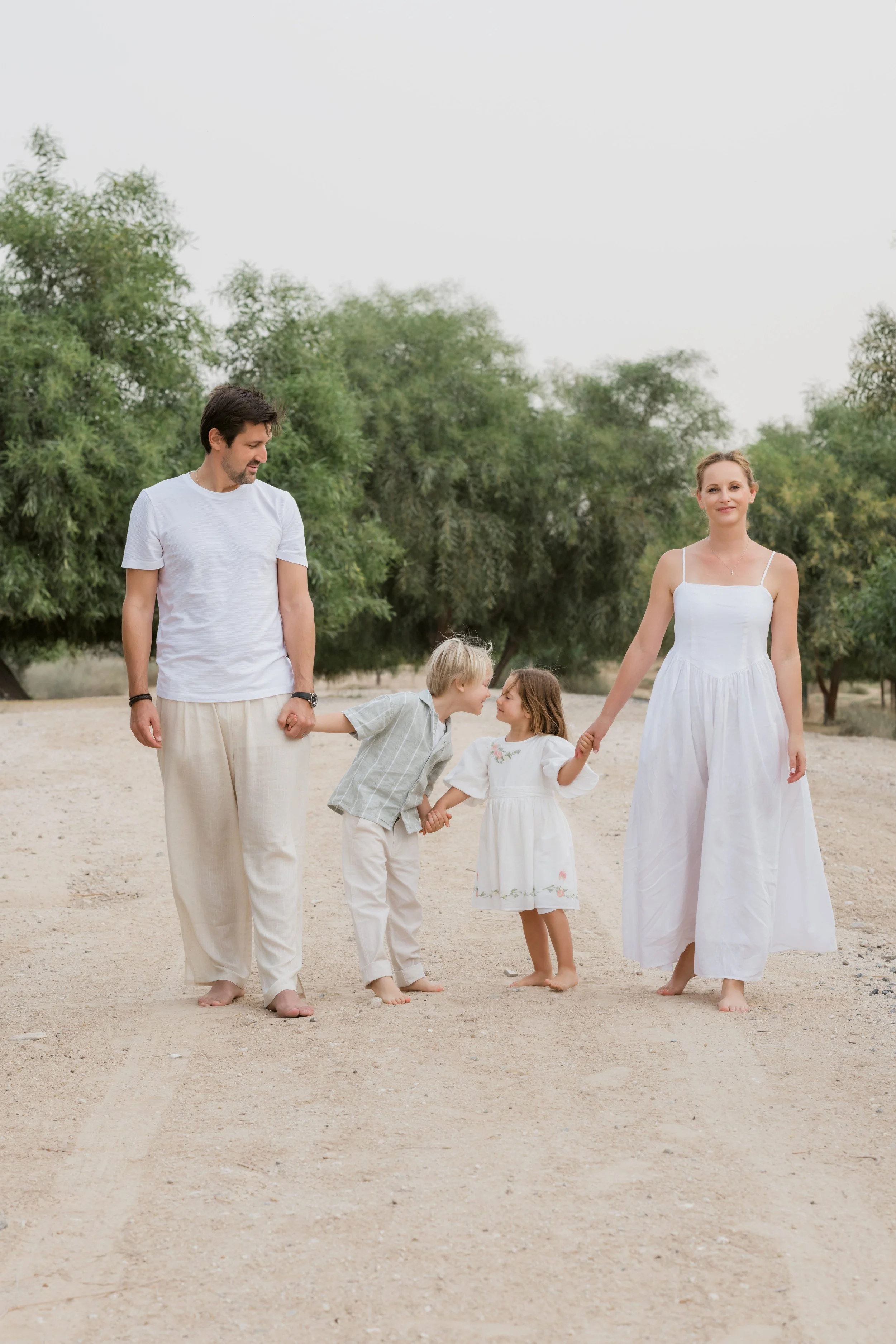 Parents walking barefoot with their children during a relaxed family photography session in Al Qudra Lakes, Dubai.