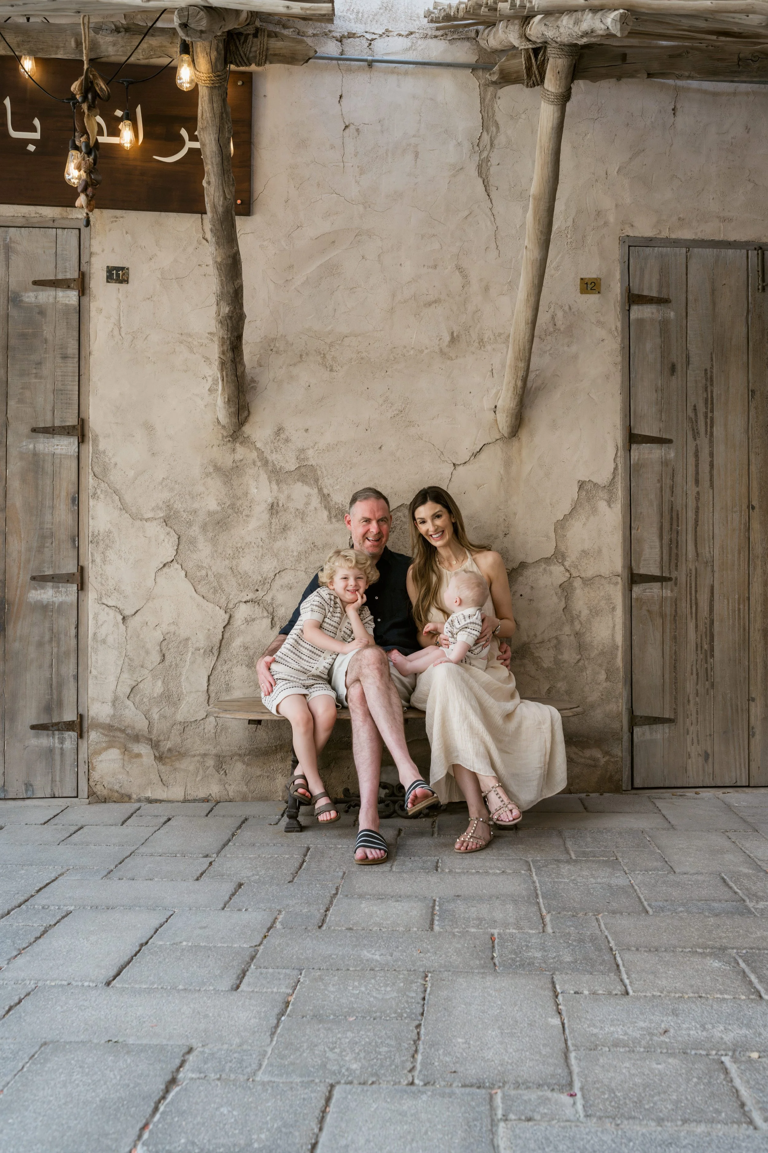 Mum, dad, toddler and baby seated closely together on a bench, smiling during a Dubai family shoot