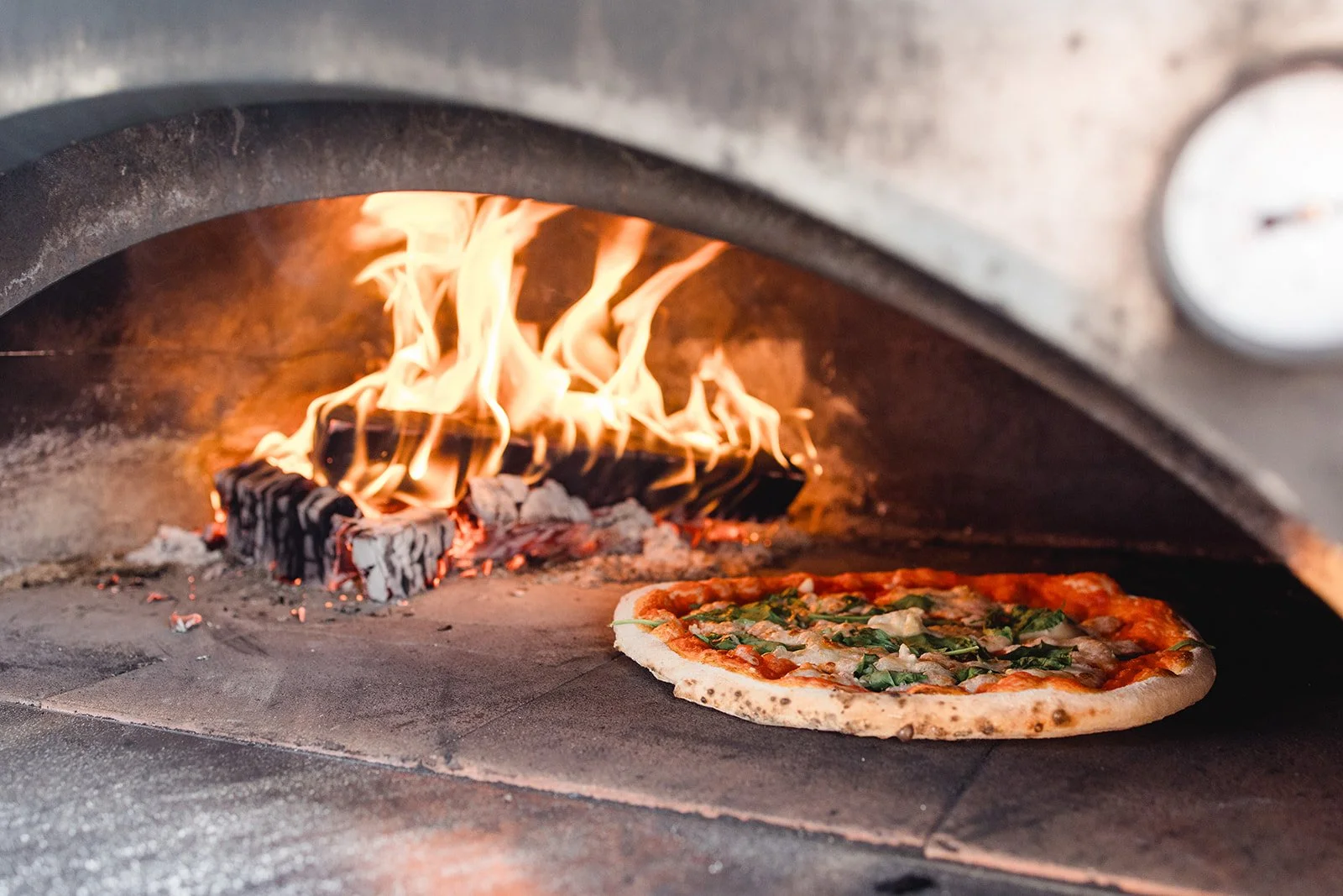 Eine Pizza in einem Holzofen mit brennendem Feuer im Hintergrund.