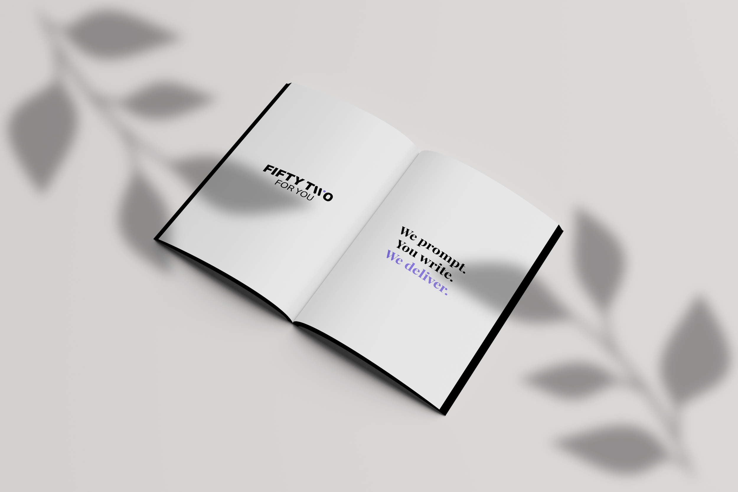 Open book with black-bordered white pages, displaying text 'Fifty Two for You' on the left page and 'We prompt. You write. We deliver:' on the right page, on a light surface with a gray leafy branch shadow in the background.