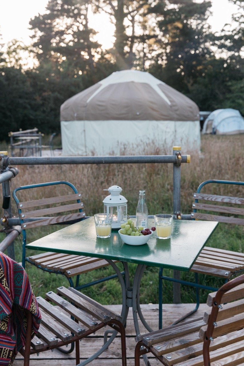 Outdoor table with juice glasses and grapes on a patio, surrounded by wooden chairs and a yurt in the background.