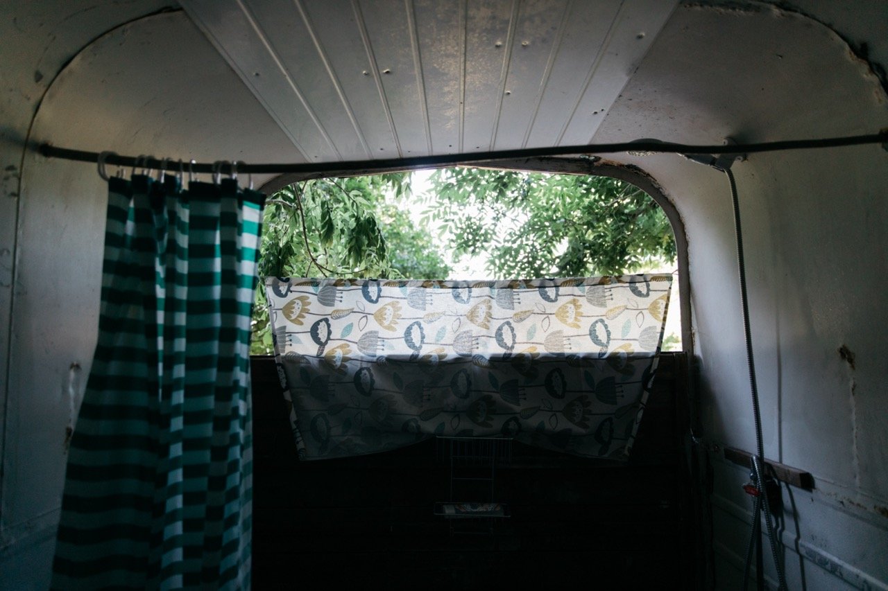Interior of a vehicle or trailer with a striped curtain and patterned cloth, trees visible outside the window.