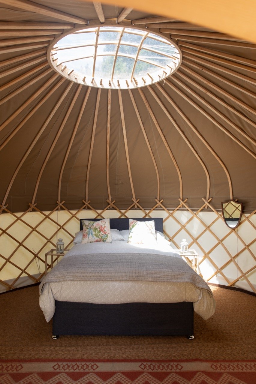 Interior of a yurt with a bed, floral pillows, and a skylight.