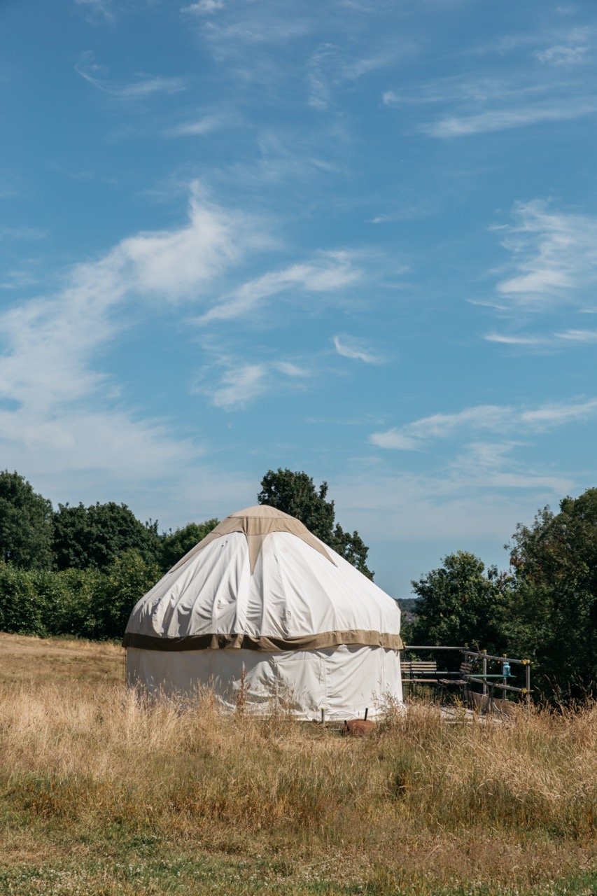 A traditional yurt standing in a grassy field under a blue sky with scattered clouds.