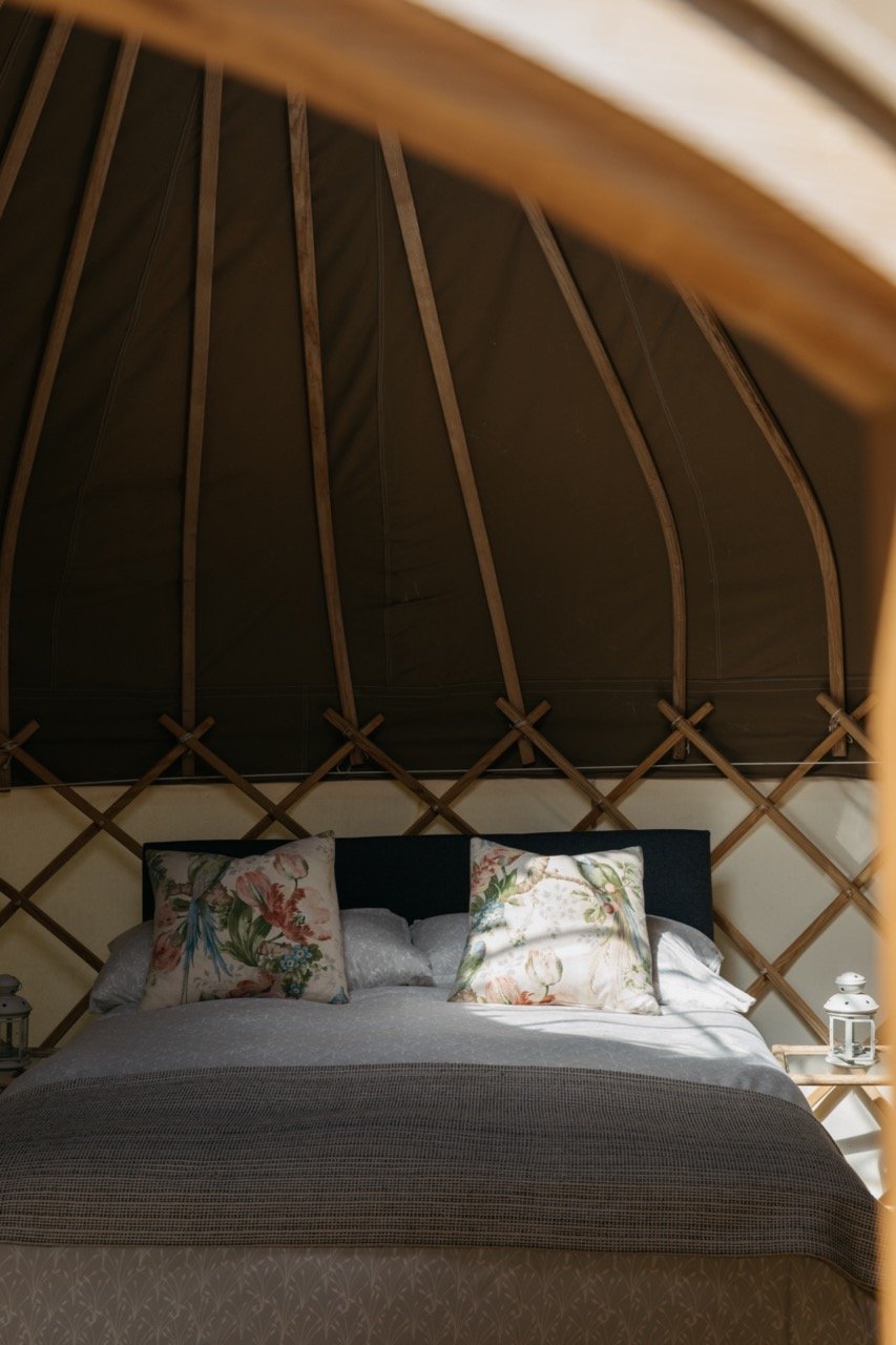 Interior of a yurt with a bed, floral pillows, and wooden lattice walls.