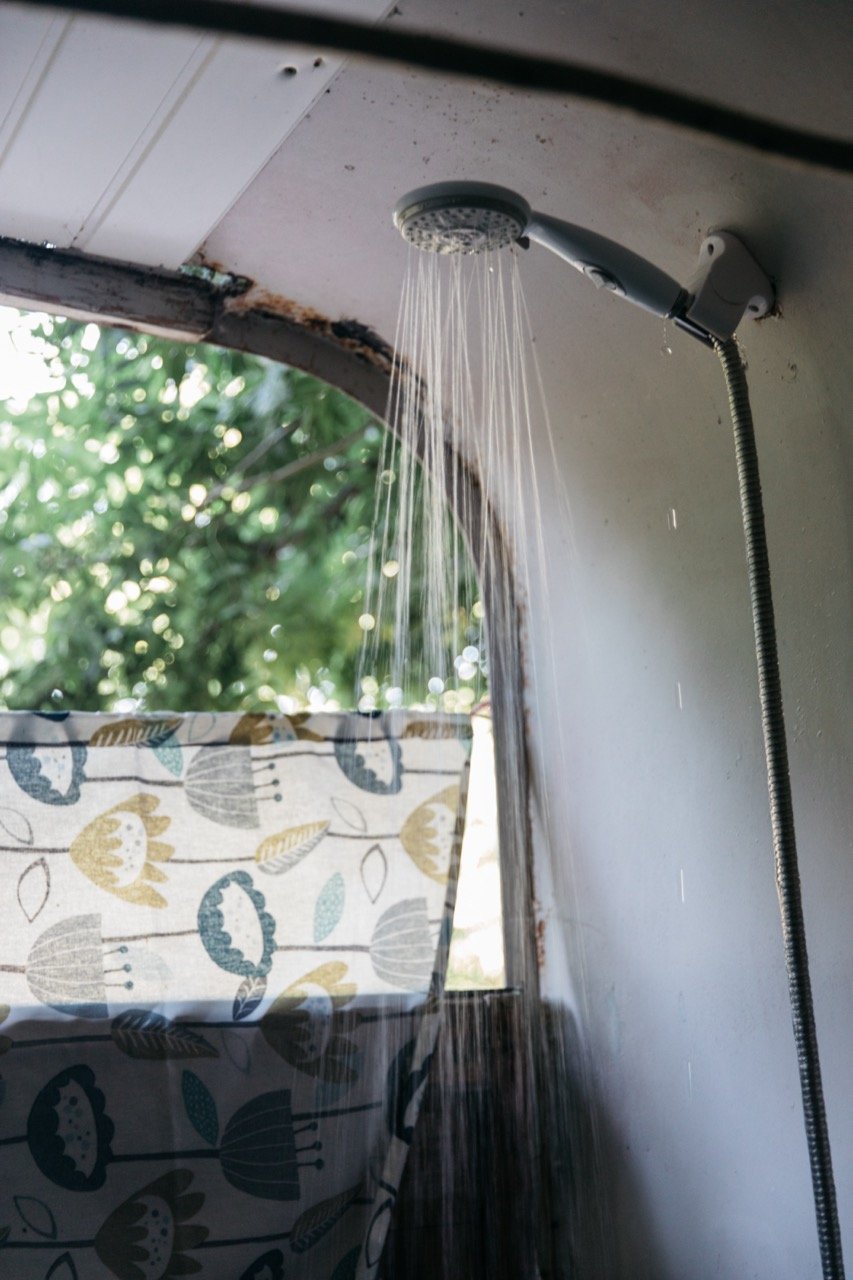 Shower head with water running in outdoor setting, floral fabric curtain.