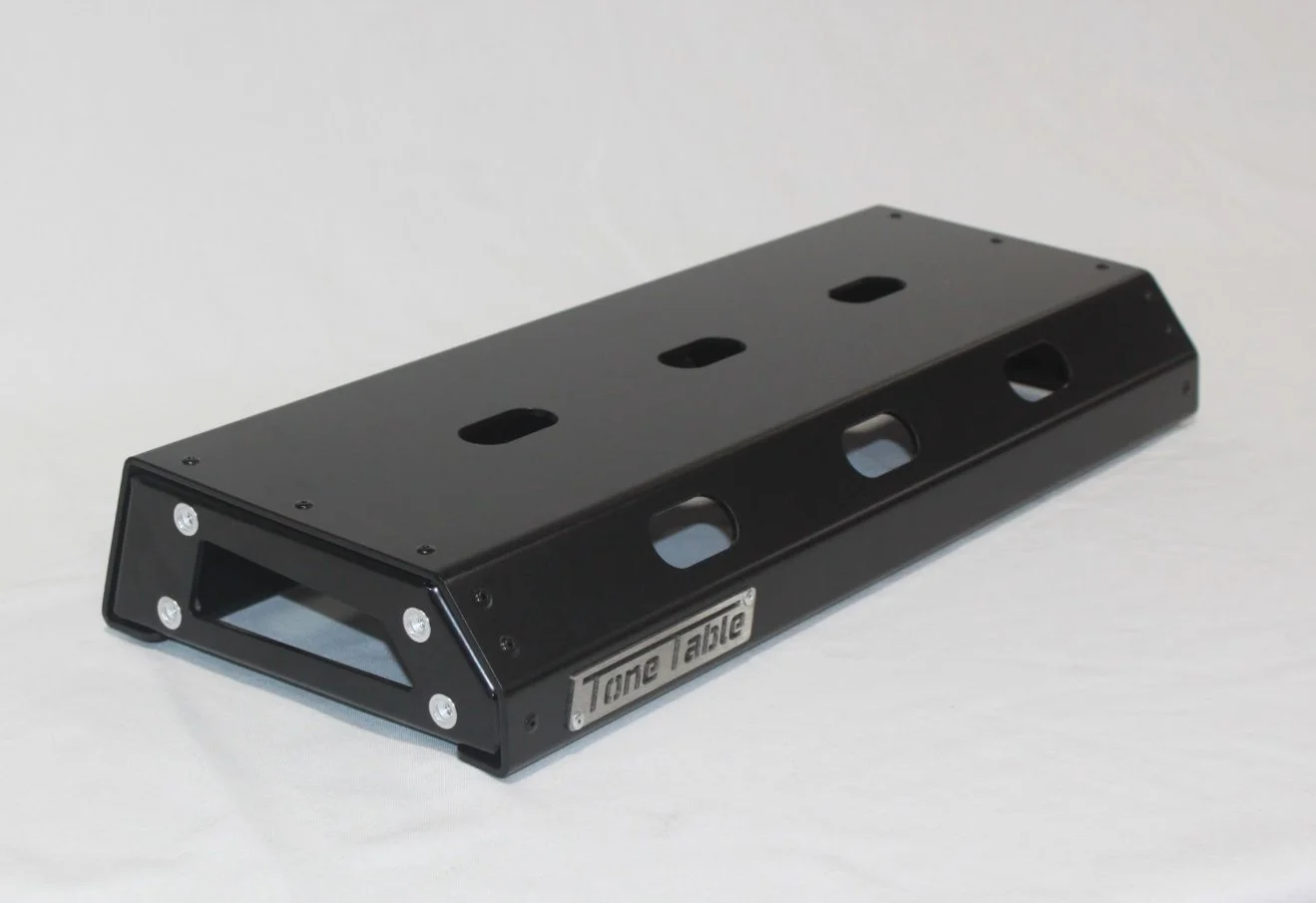 A black metal tone pedal with cutouts and a metal label reading 'Tone Jim' on the side, resting on a white surface.