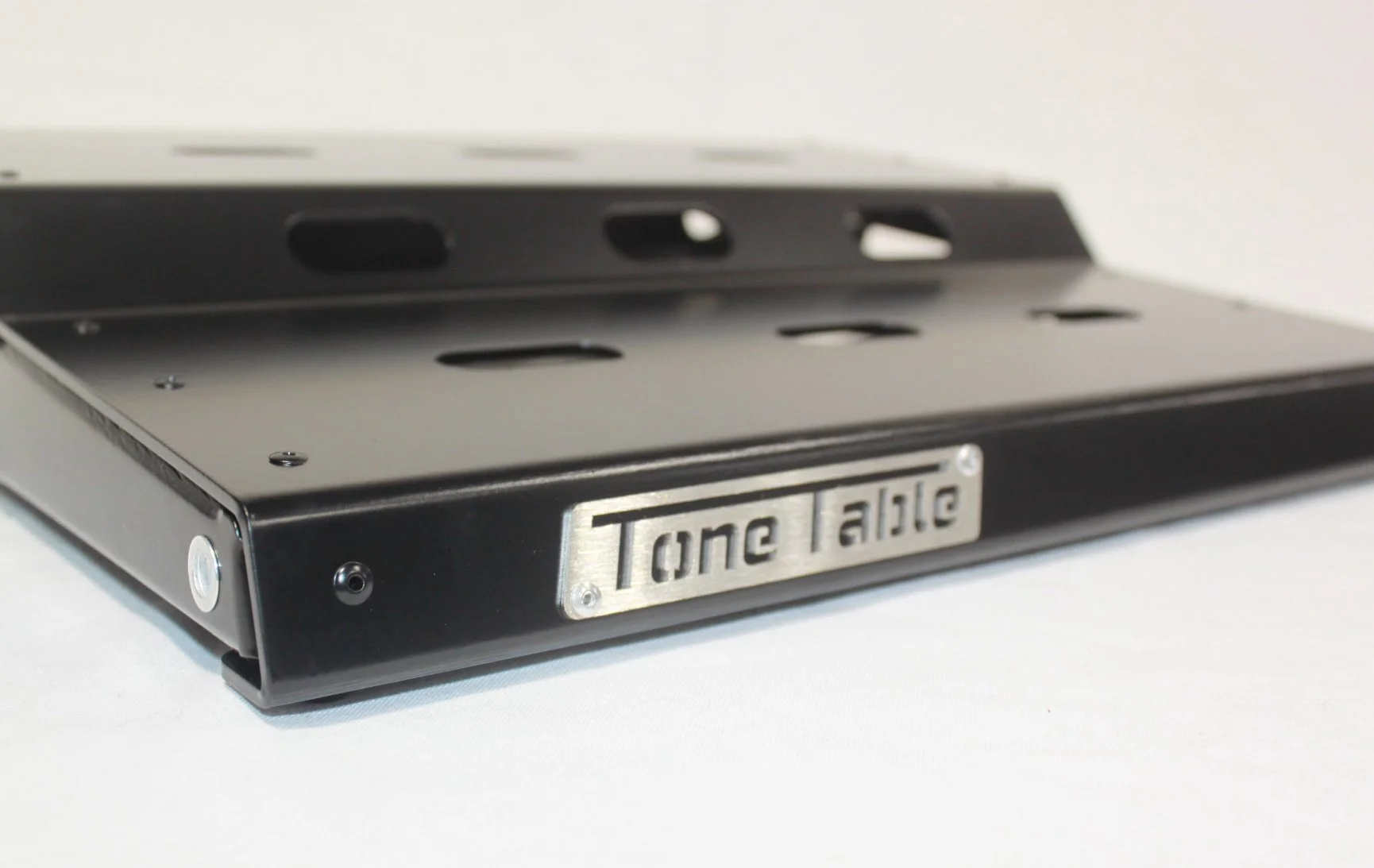 A black metal Tone Table guitar effects pedal with a metal label reading "Tone Table" on the front, shown on a white surface.