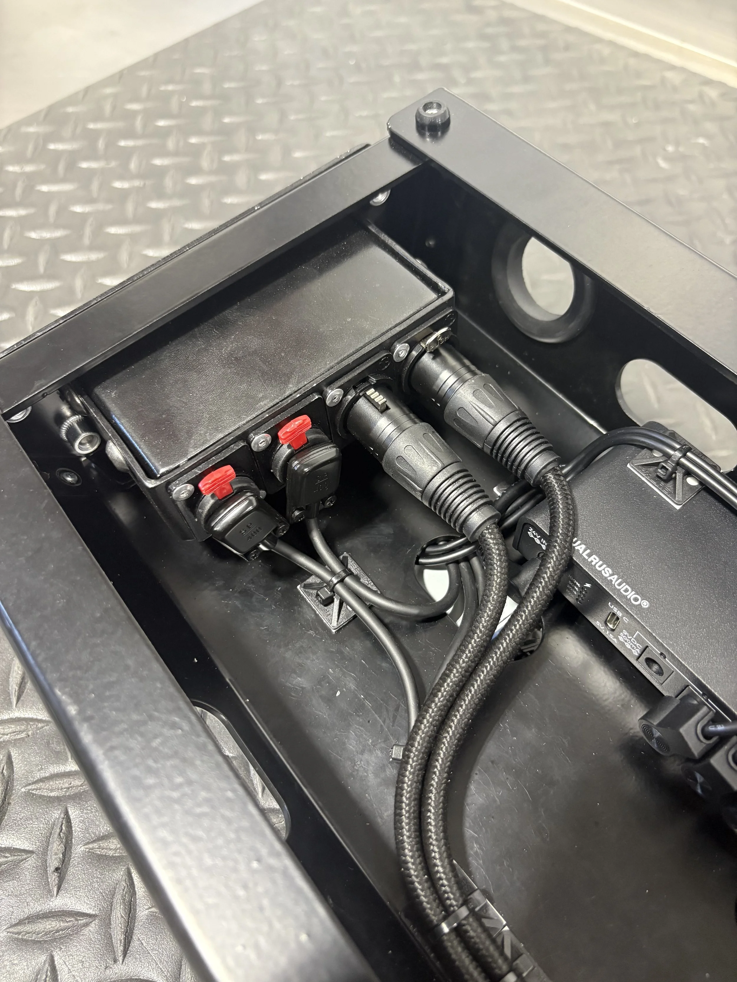 Close-up of an electronic equipment rack with power strips, cables, and audio equipment inside a metal frame.