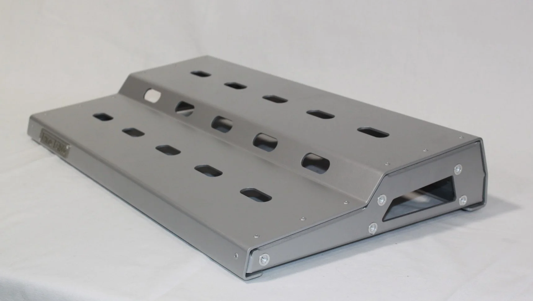 A silver metal pedal with multiple holes, likely for adjusting position, set on a white surface against a plain background.