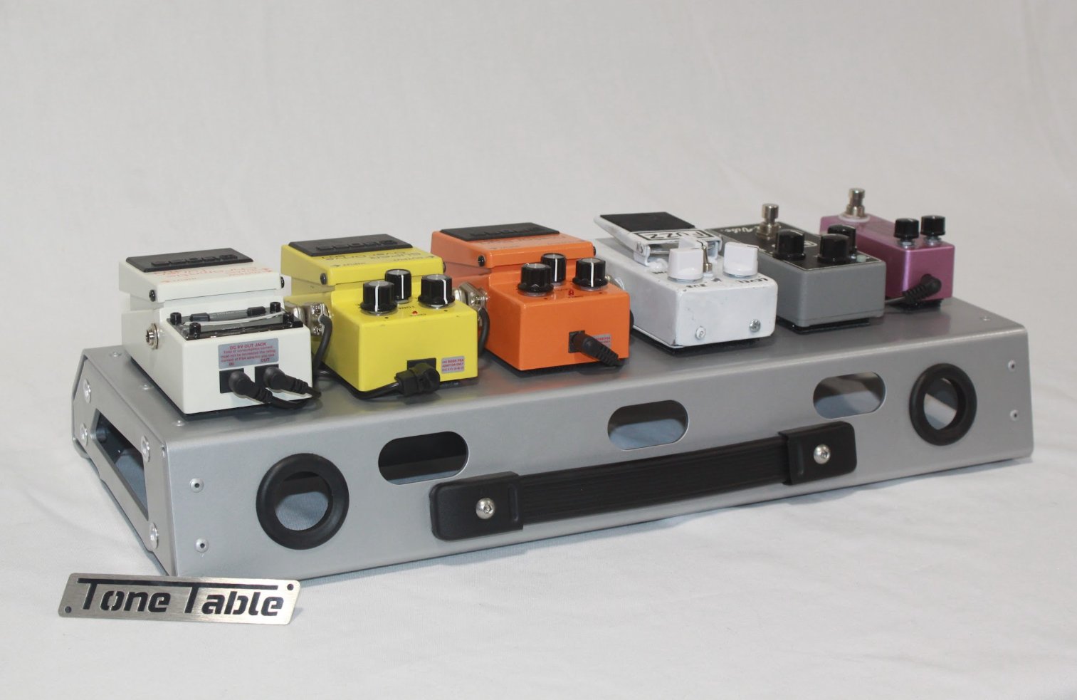 A collection of guitar effect pedals in various colors on a metal pedalboard labeled Tone Table.