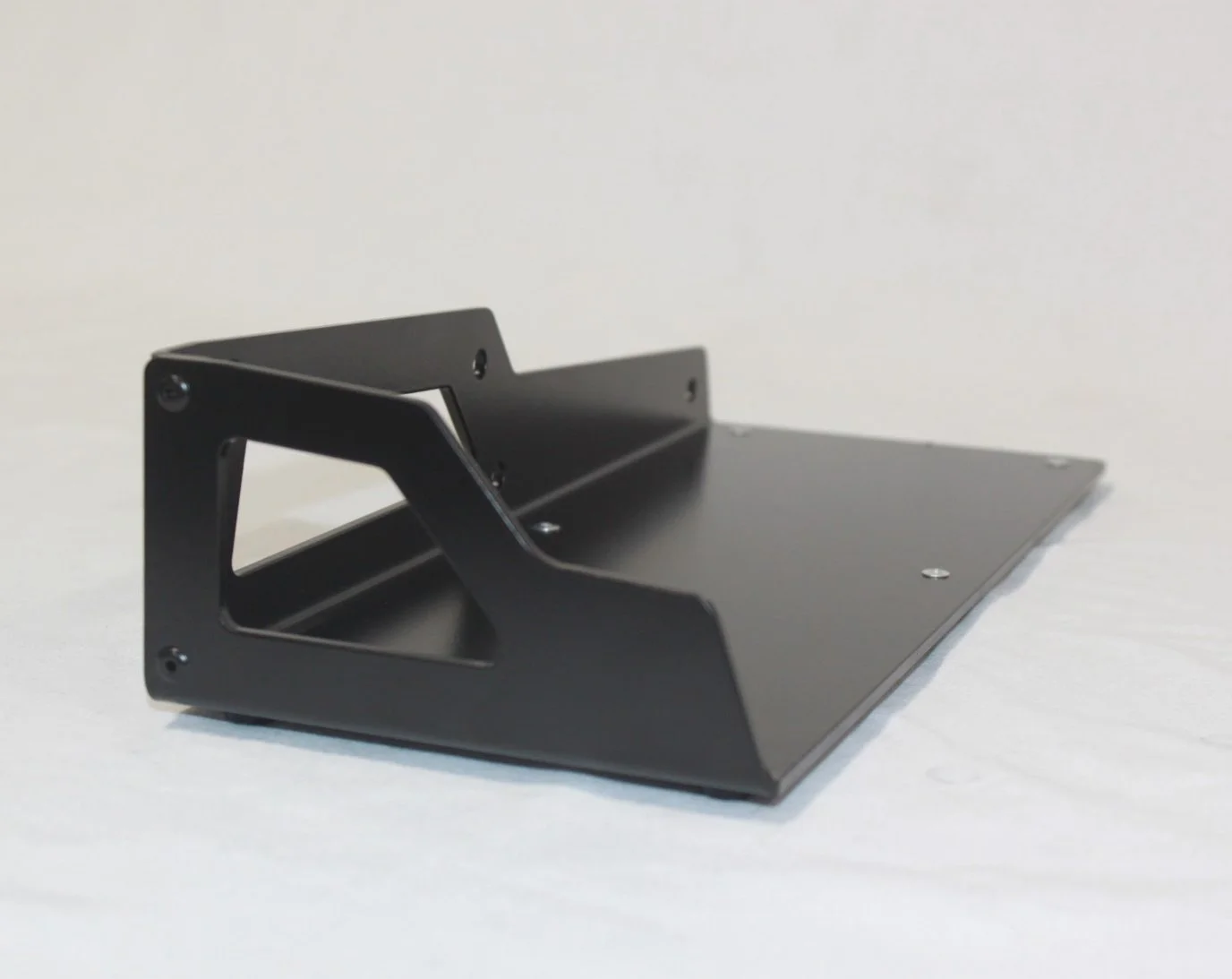 A black metal object with a sloped base and a raised, angled section, possibly a stand or mounting bracket, on a white background.