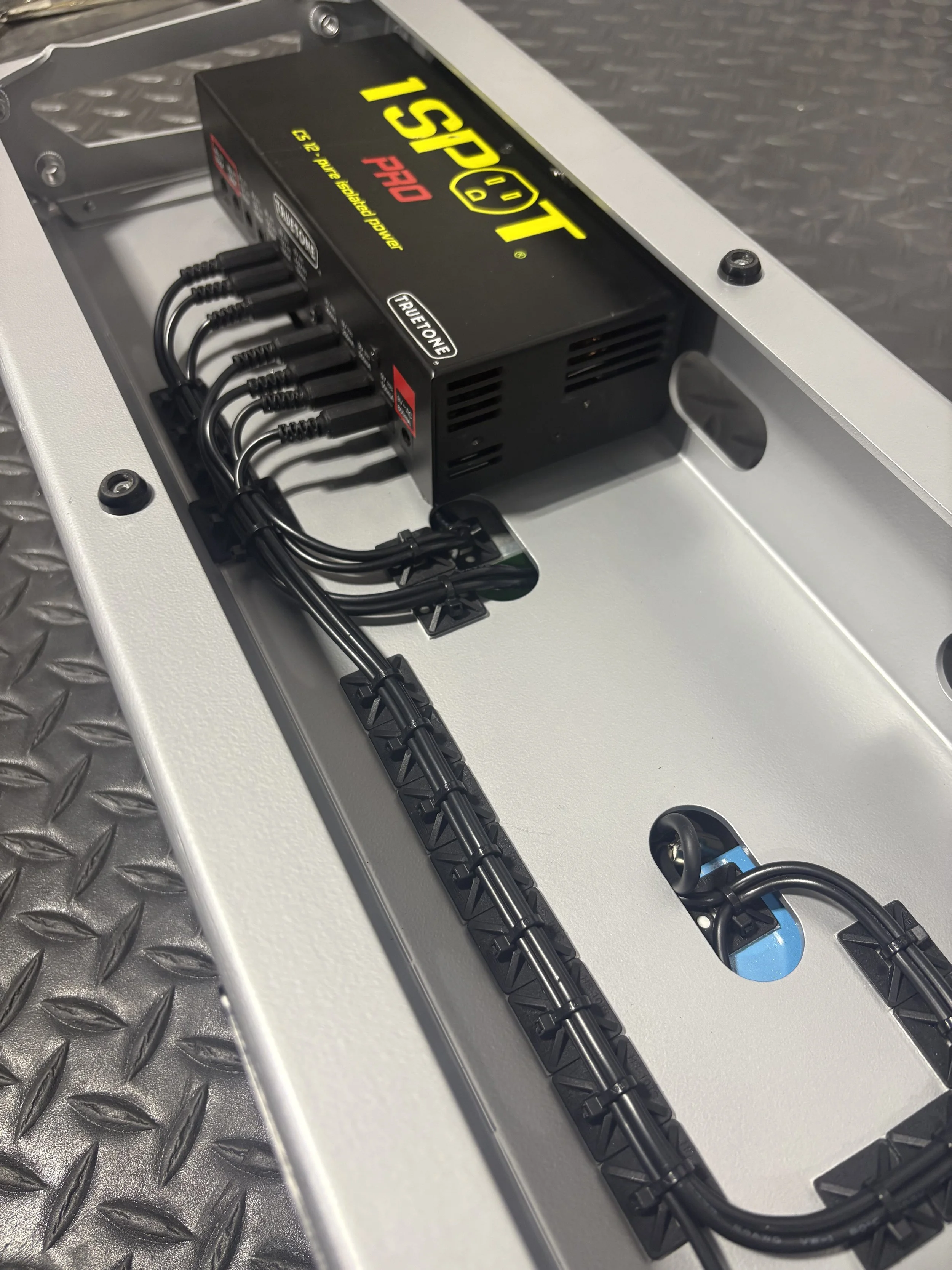 A power supply unit installed inside an electrical panel or equipment cabinet, with multiple black cables connected to it, on a metallic surface with a textured, diamond plate pattern.