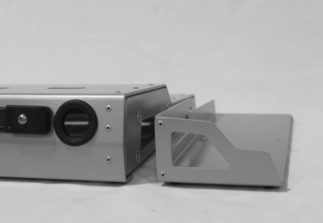 A metallic mechanical device with a black circular opening and black component on a light background.