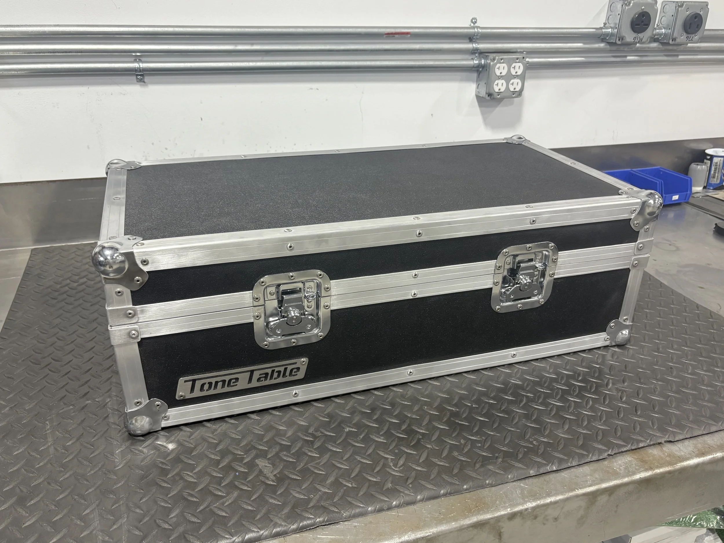 A black flight case with metal edges and handles, labeled 'Tone Tools,' placed on a metallic work surface in an industrial or workshop setting.