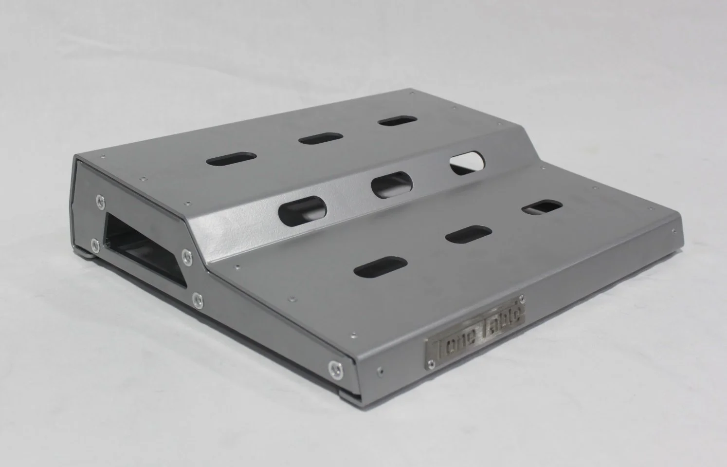 A metallic device with a sloped design and multiple oval and rectangular holes on top, with a label or serial number on one side.