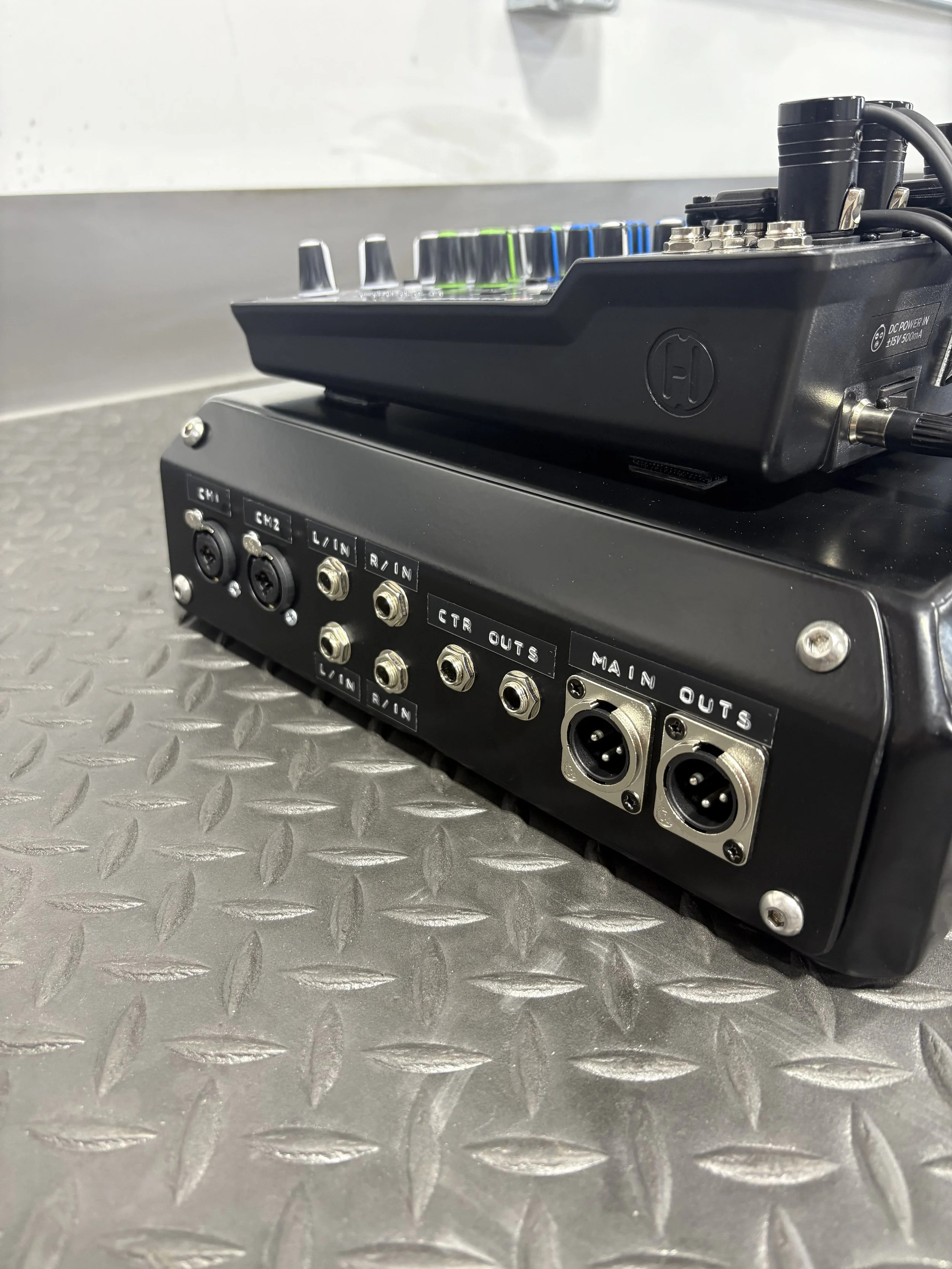 Close-up of an audio mixer with various input and output ports, set on a metal surface.