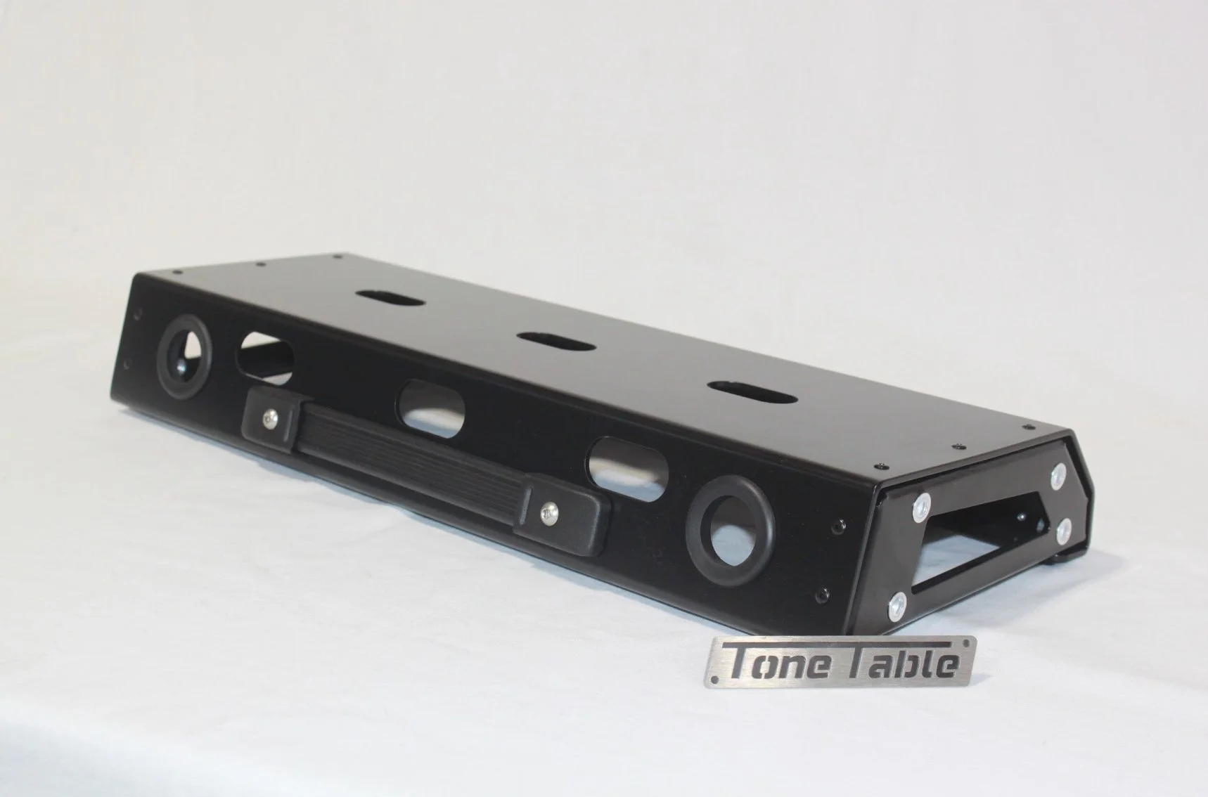 Black tone table with circular and rectangular cutouts, placed on a white surface, with a metal label reading 'Tone Table' in front of it.