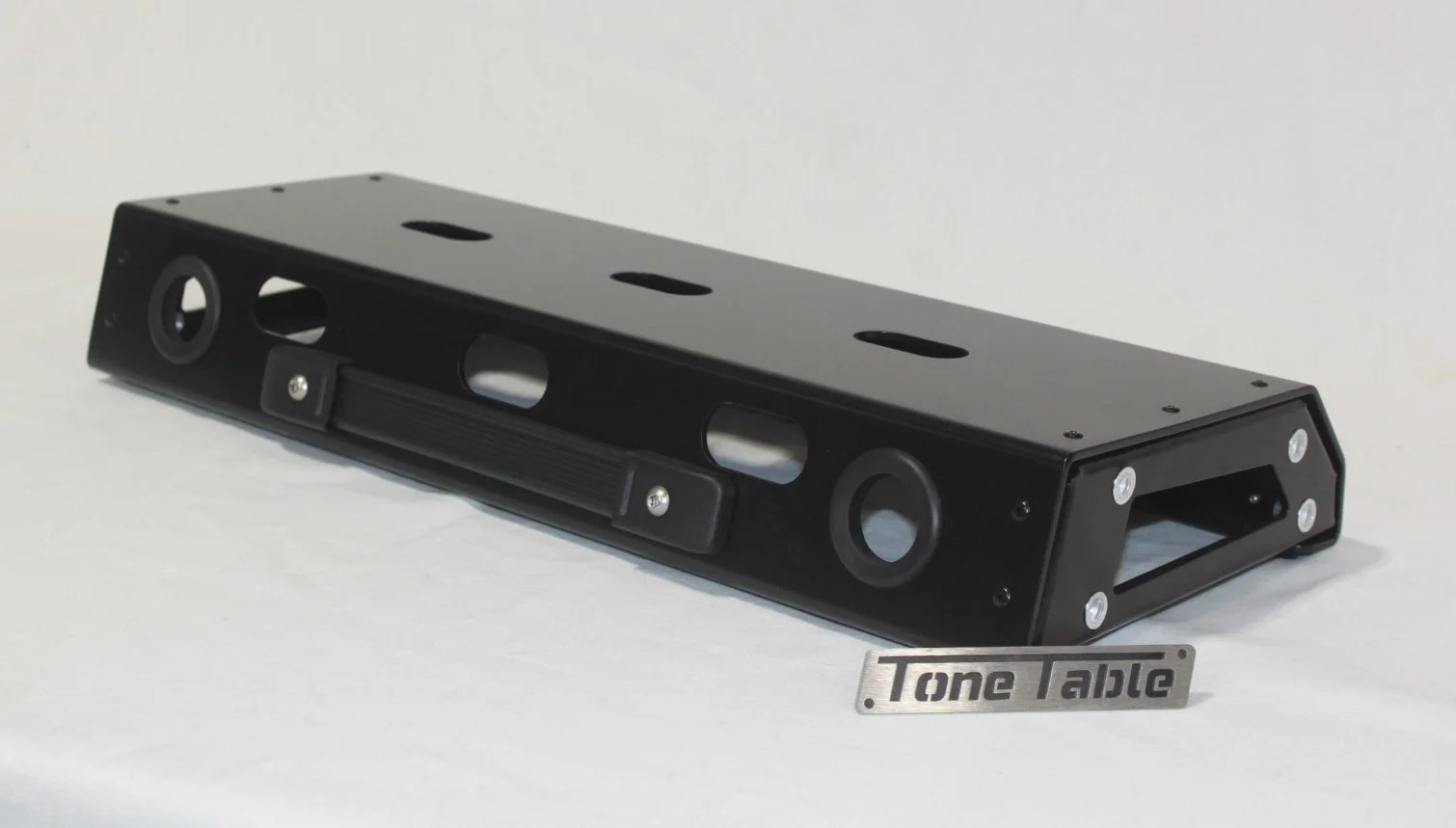 A black tone table with multiple circular and rectangular openings, mounted on a white surface, with a small metal plaque labeled "Tone Table" in front of it.