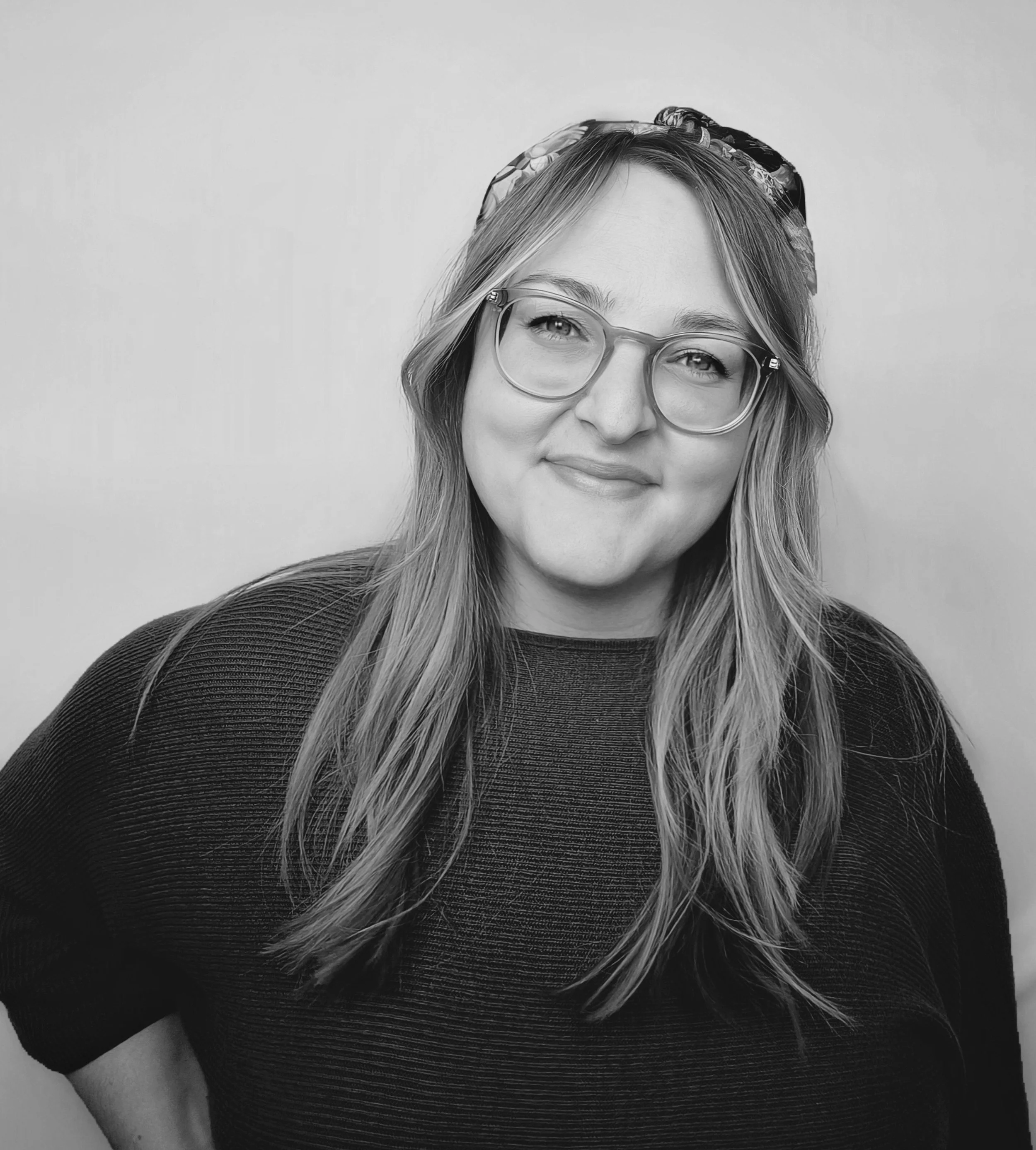 Beth, Operations Lead at The Path, with glasses, long wavy hair, a headband, and a relaxed smile, standing against a plain light background.