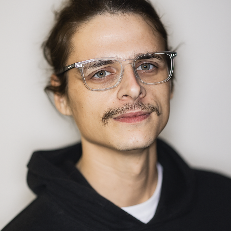 Young man with glasses and mustache smiling, wearing a hoodie.