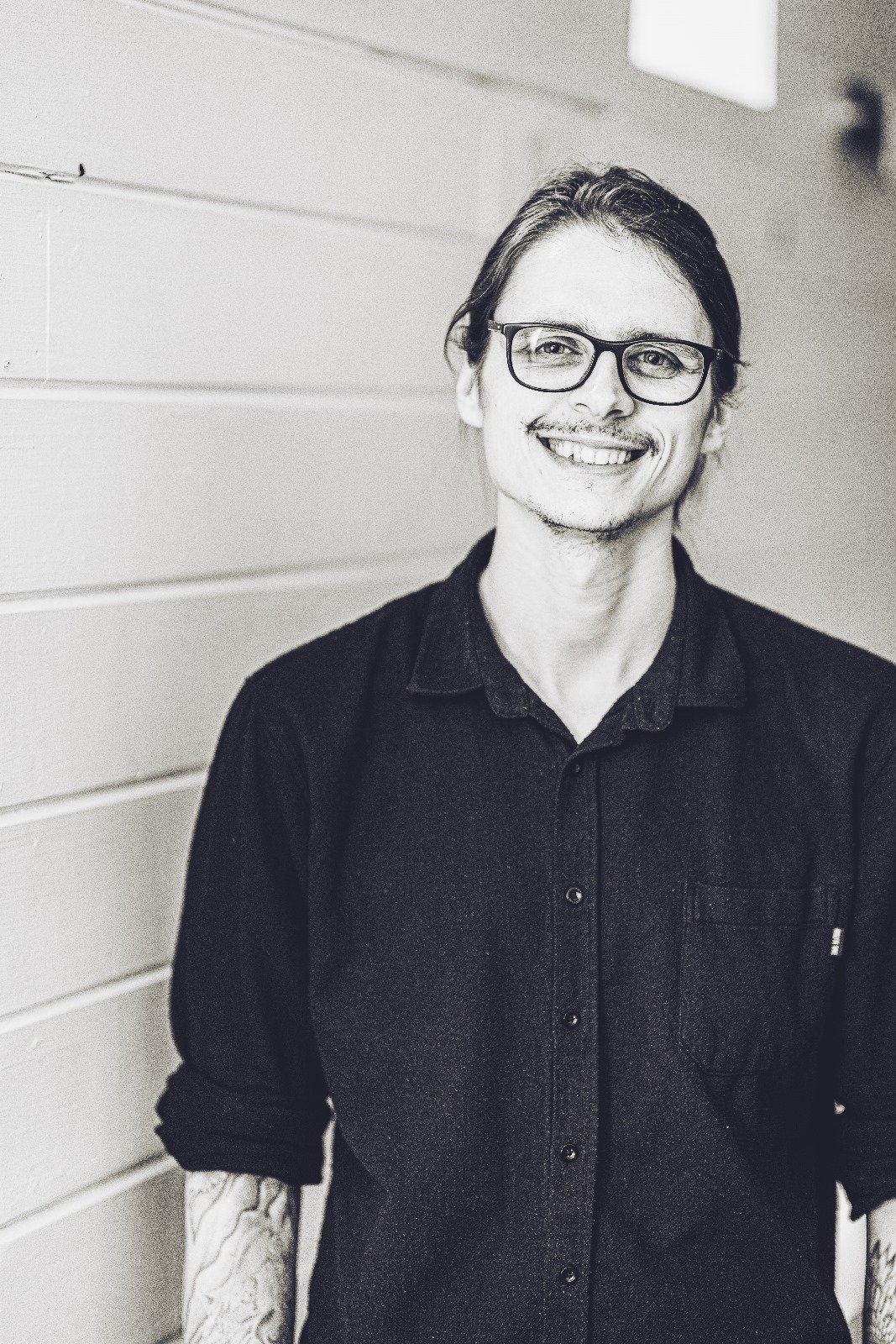 Chris, Influencer Strategy Lead at The Path, smiling wearing glasses and a dark button-up shirt, standing against a wooden wall.
