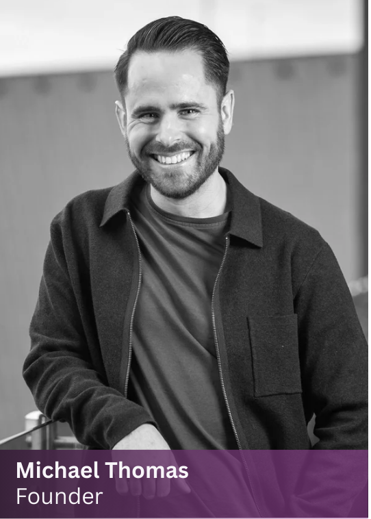 Michael, founder of The Path, smiling and wearing a dark jacket over a T-shirt, leaning on a surface in an outdoor setting.