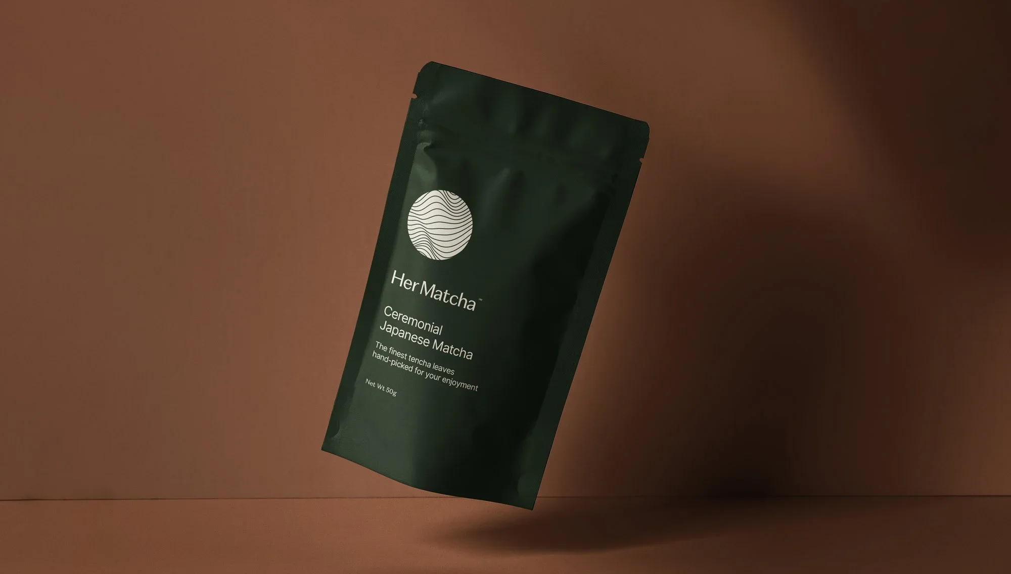 Dark green packet of HerMatcha ceremonial Japanese matcha tea floating against a brown background.