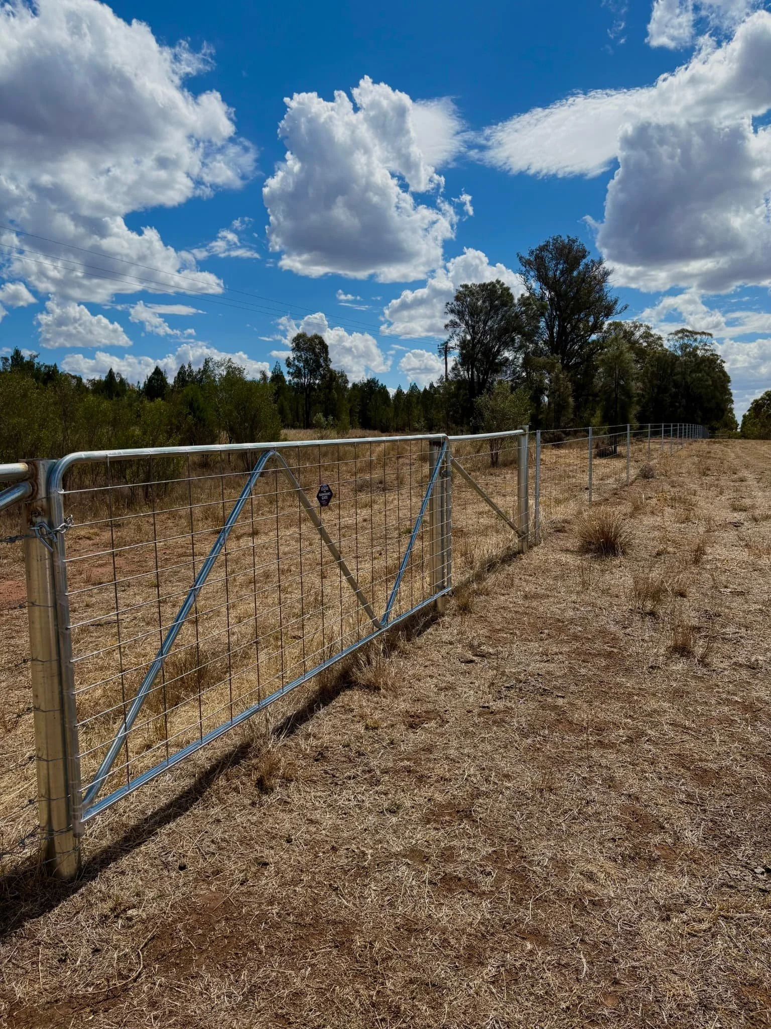 Farm gate and end assembly on hinge joint fence across dry rural paddock, agricultural fencing contractors NSW