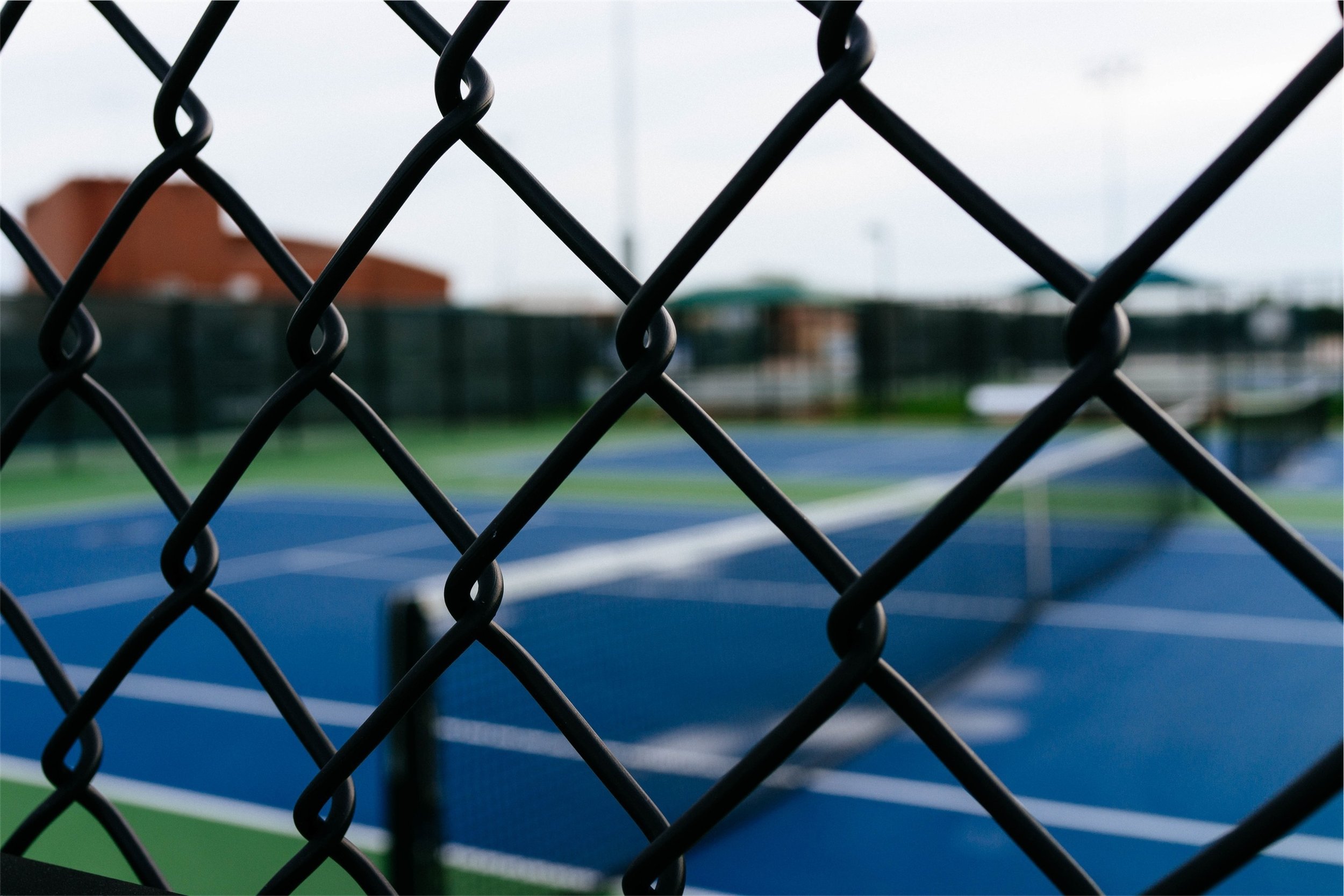 Black chainwire tennis court fencing close-up with blue hard court surface, tennis court fencing Northern Rivers NSW