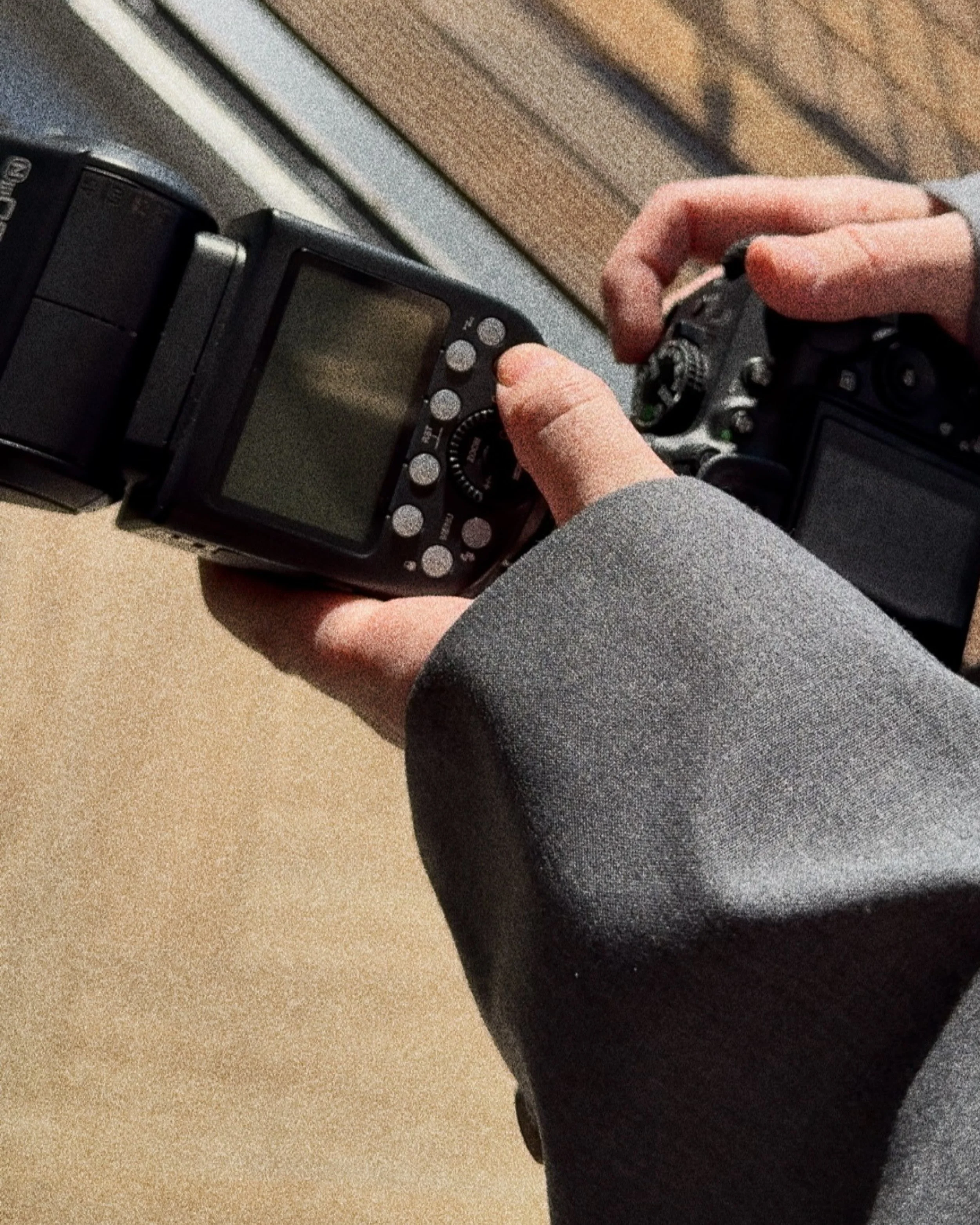 Person holding a digital camera with an external flash unit attached, adjusting camera settings.