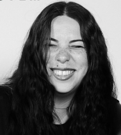 Black and white photo of a woman with long, wavy hair smiling and winking.