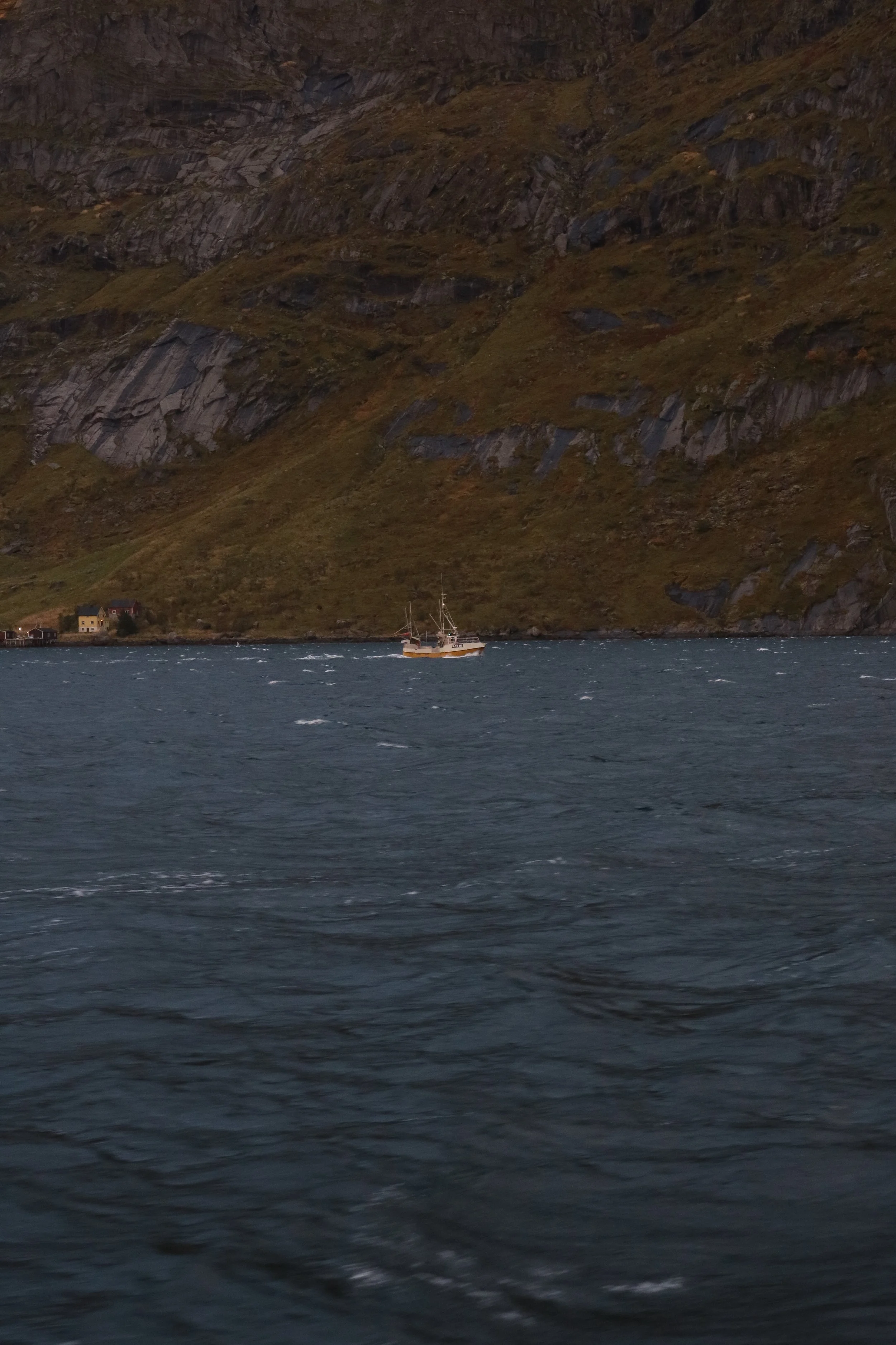 A boat sailing on a deep blue body of water with a rugged Norwegian mountainside in the background.