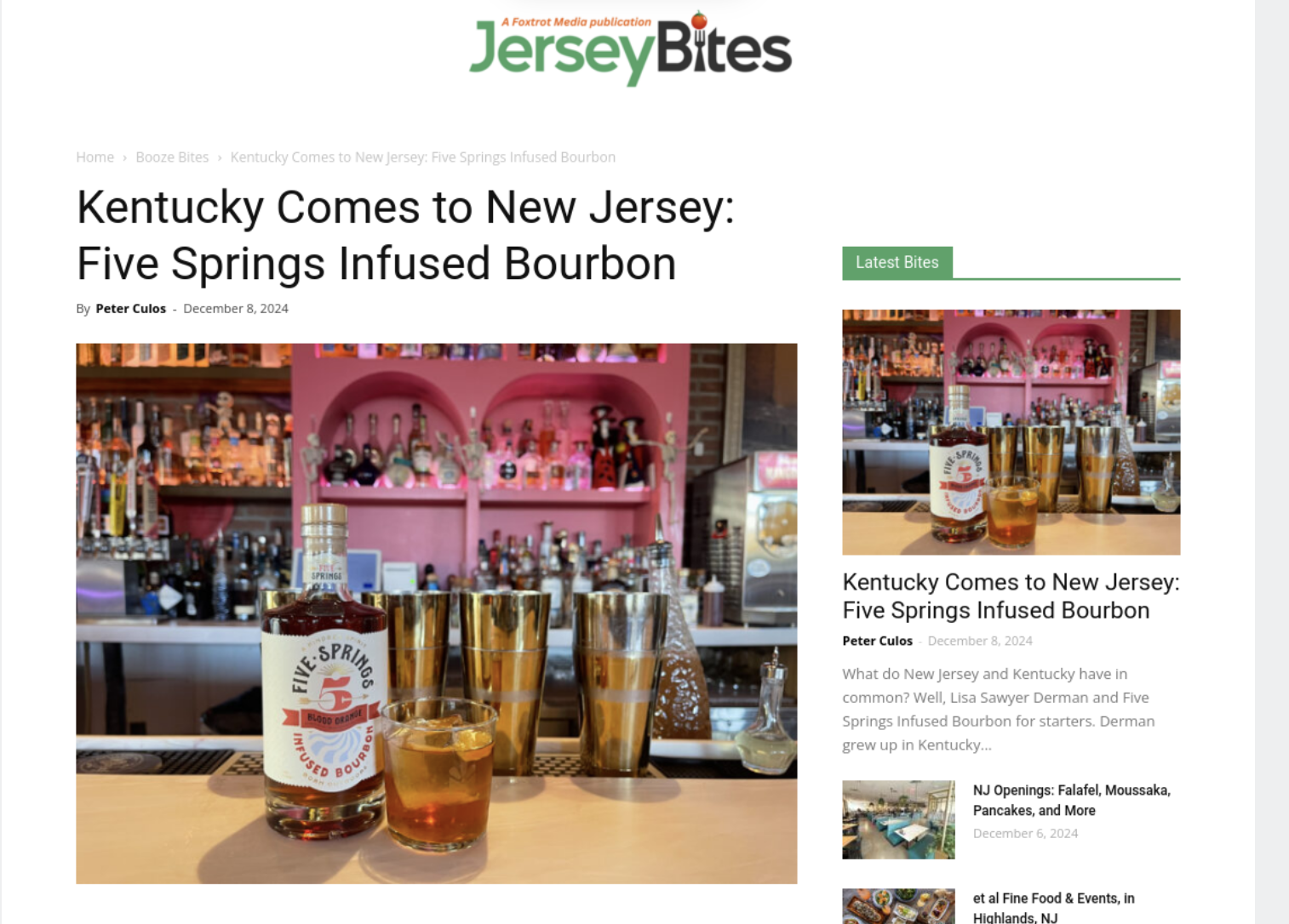 A bar with a bottle of Bourbon whiskey and two glasses filled with bourbon on the counter, with shelves of liquor bottles and barware in the background.
