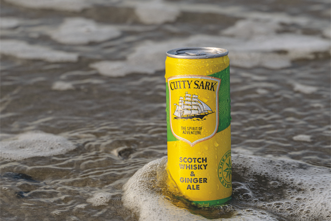 A can of Cutty Sark Scotch Whisky and Ginger Ale partially submerged in the ocean water with foam around it.