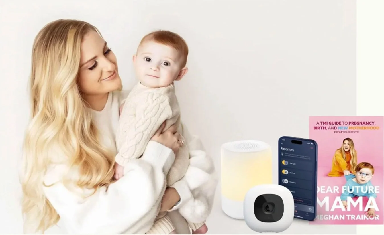 A woman with long blonde hair holding a young child with red hair and glasses, sitting next to smart home devices and a pink book titled 'Dear Future Mama'.